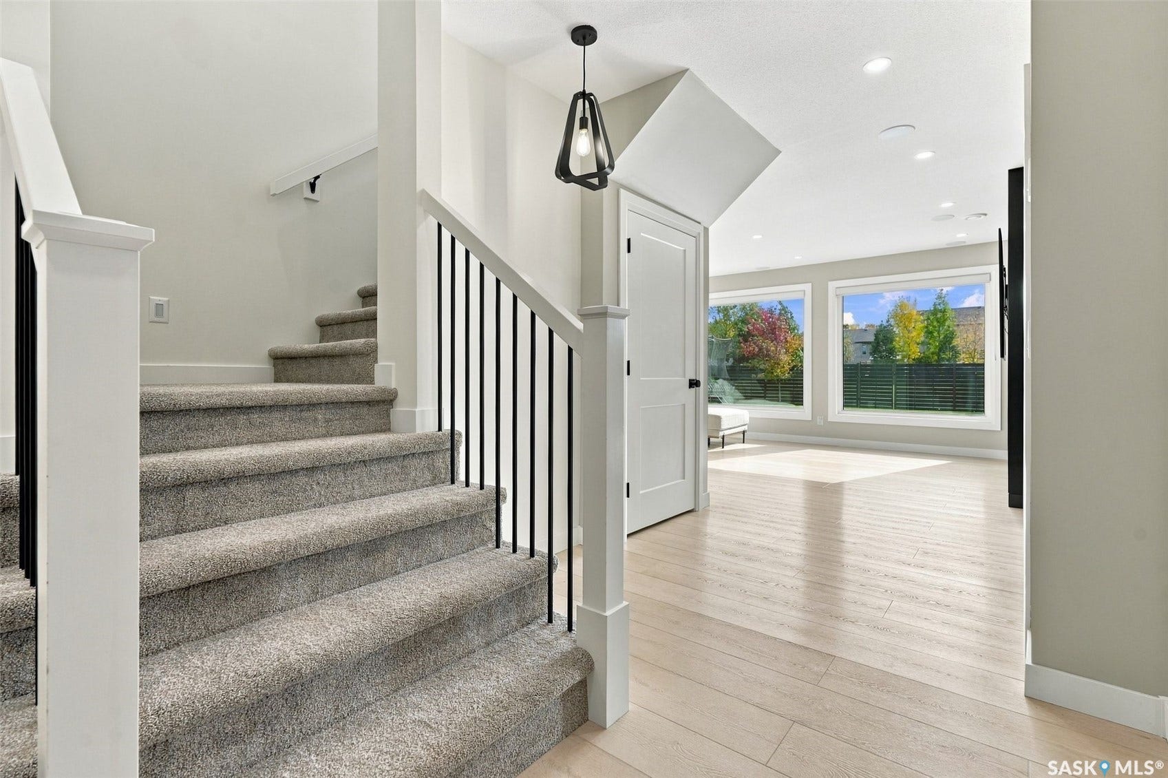 6221 Koep Avenue, Regina SK S4X 0J2 Carpeted staircase with black iron balusters, white wood newel post, wood-finish flooring, recessed lighting, and large windows