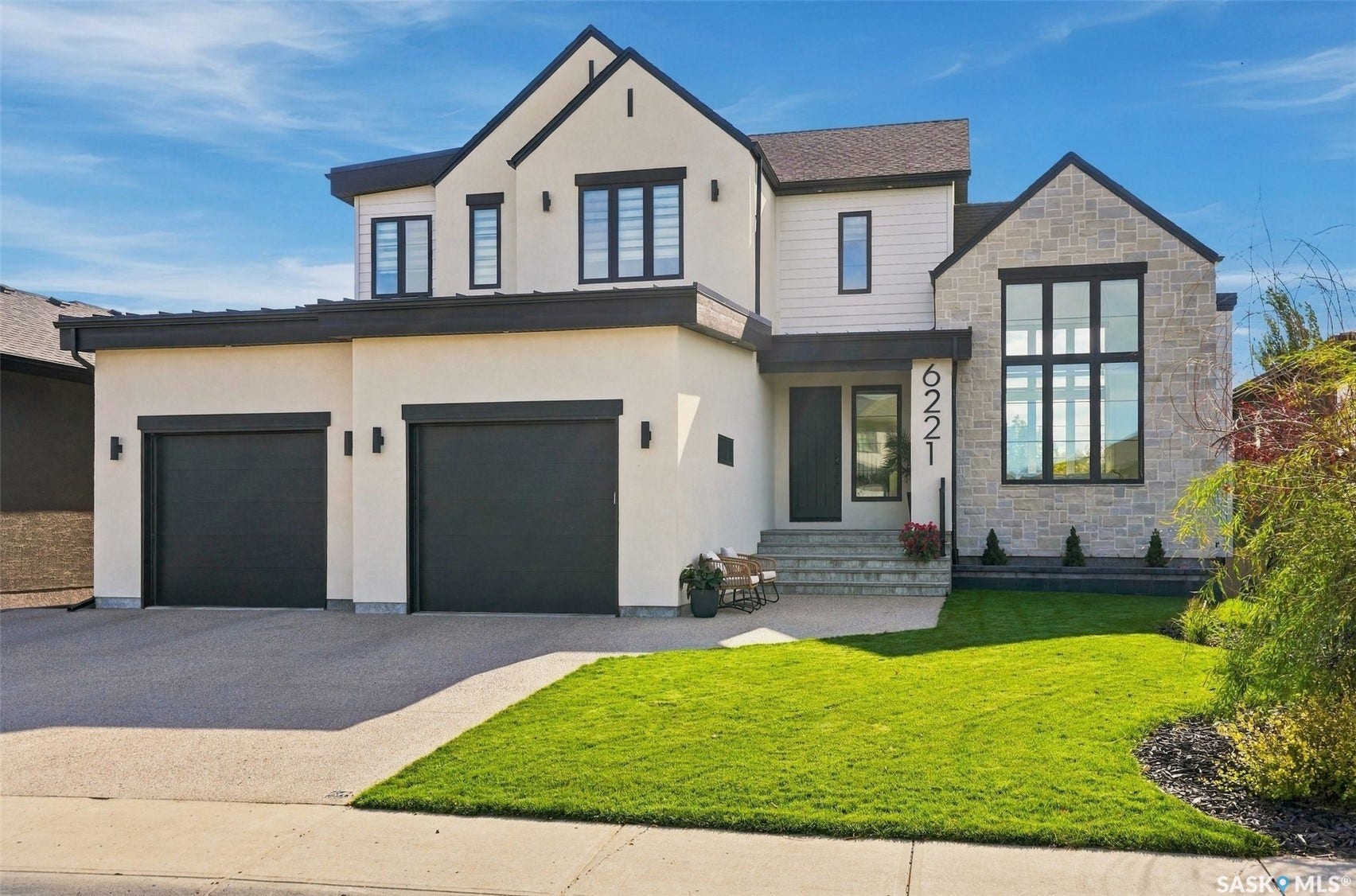 6221 Koep Avenue, Regina SK S4X 0J2 Stucco exterior with stone accent, two-car garage, mature landscaping, and multi-paned windows