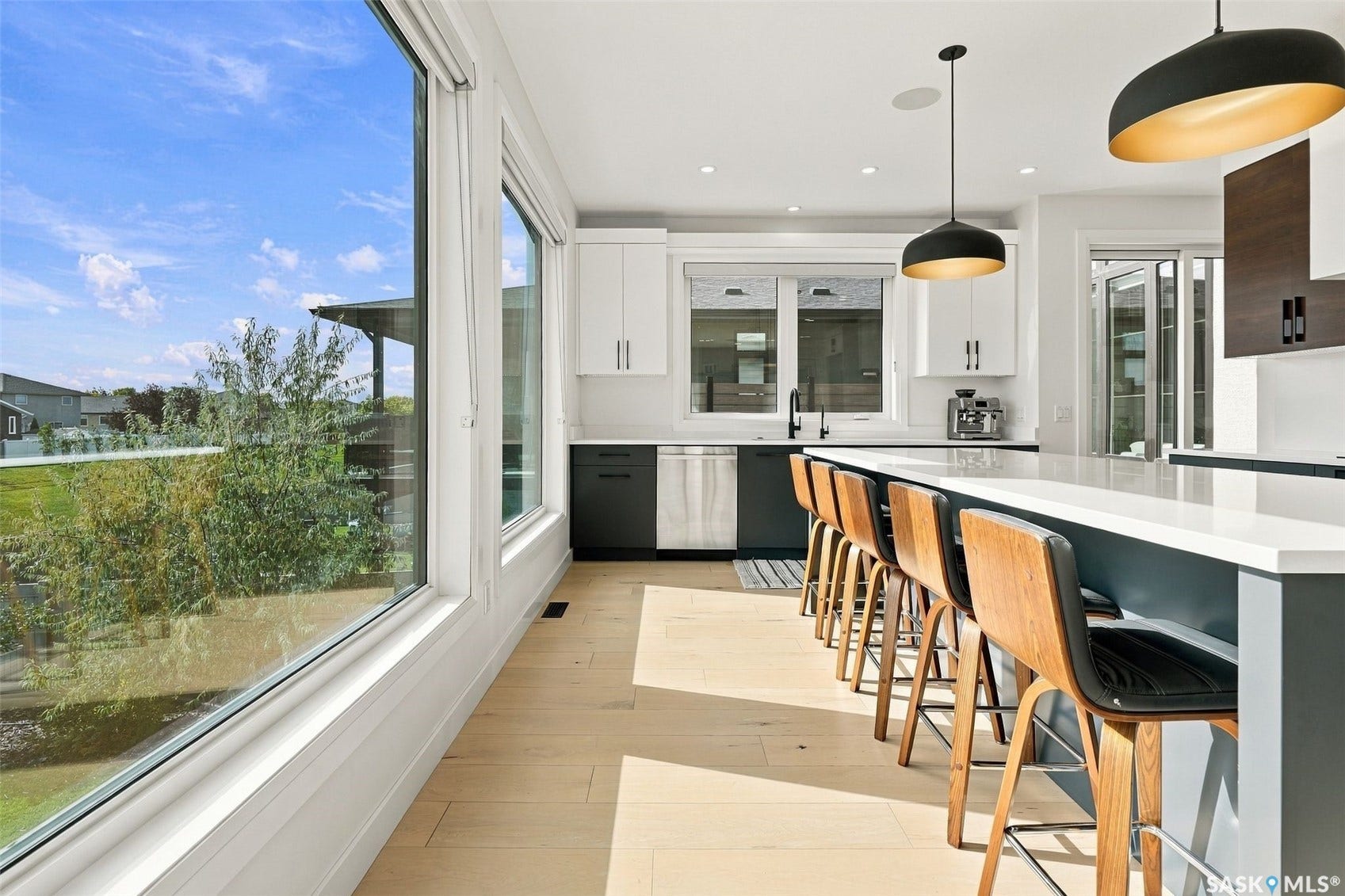 6221 Koep Avenue, Regina SK S4X 0J2 Expansive floor-to-ceiling windows, light wood-finish flooring, white upper cabinetry, dark lower cabinetry, and a large central island with seating
