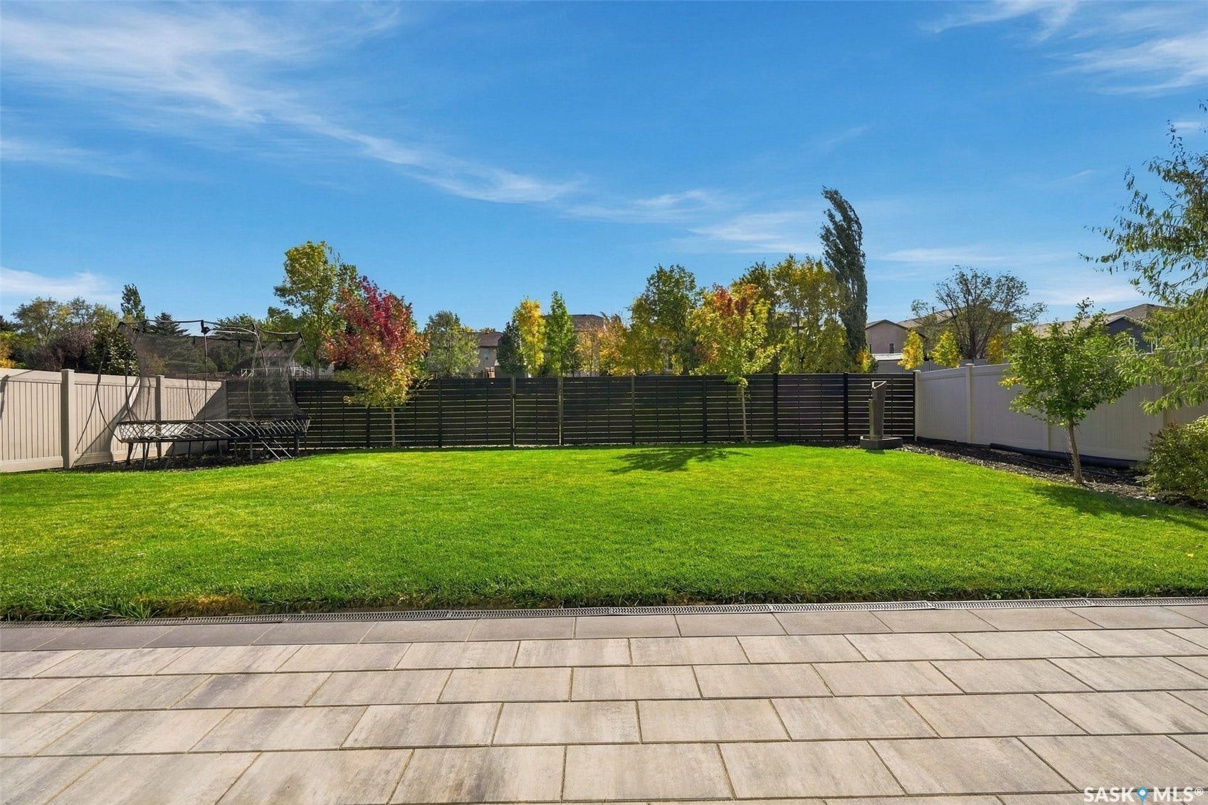 6221 Koep Avenue, Regina SK S4X 0J2 Expansive backyard featuring a large paved patio, manicured lawn, and privacy fencing