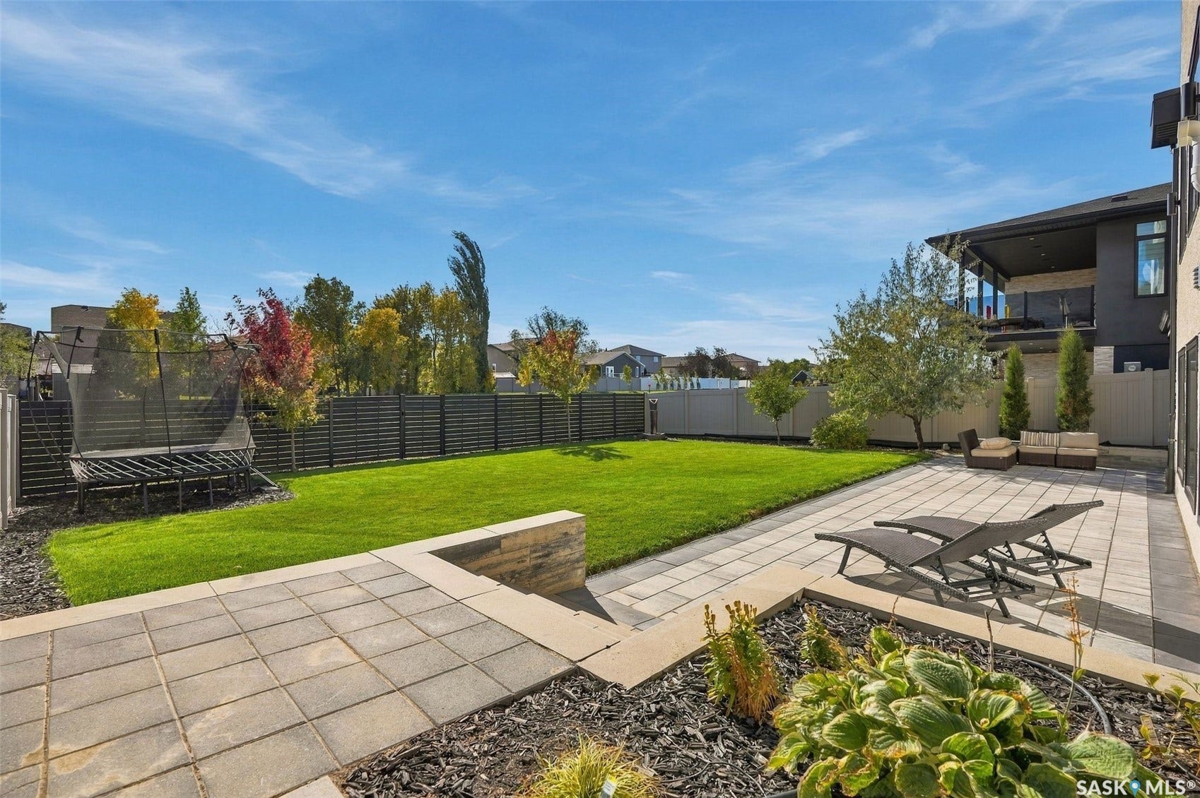 6221 Koep Avenue, Regina SK S4X 0J2 Expansive backyard featuring a manicured lawn, a large paver patio, stone retaining walls, and planted garden beds