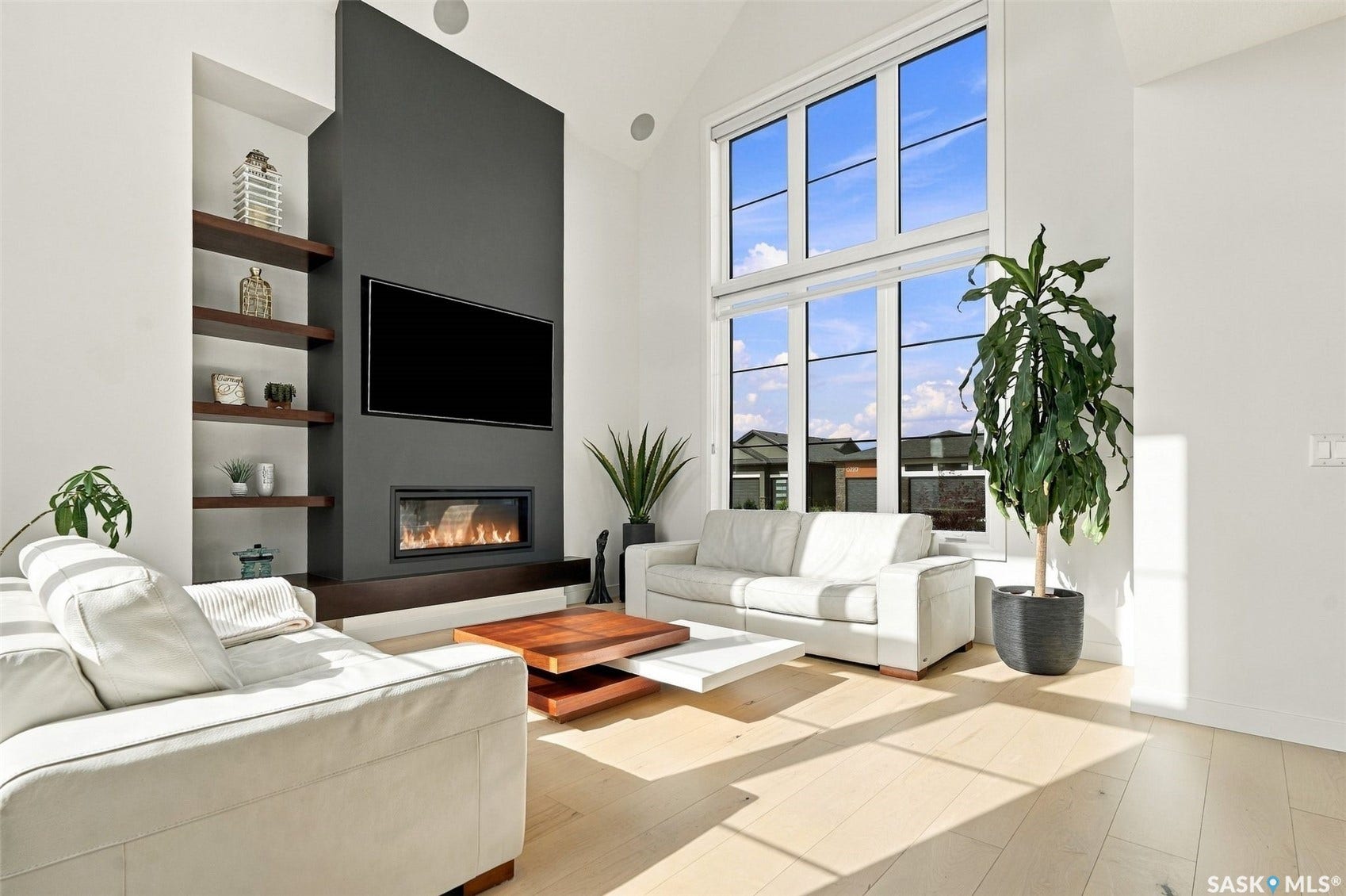 6221 Koep Avenue, Regina SK S4X 0J2 Vaulted ceiling, full-height fireplace with integrated media, built-in shelving, expansive windows, and light wood-finish flooring