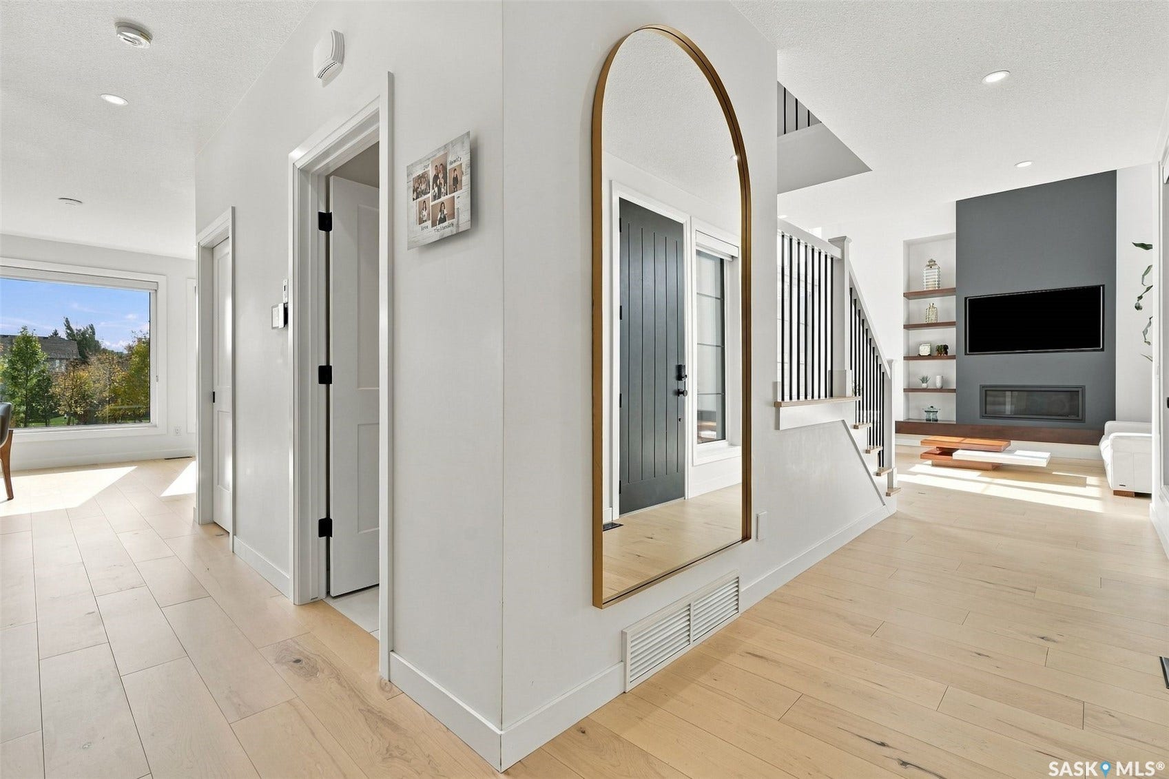 6221 Koep Avenue, Regina SK S4X 0J2 Light wood-finish flooring throughout, modern staircase with dark risers and light wood treads, a large window providing natural light, a dark accent wall with a built-in linear fireplace, and recessed lighting