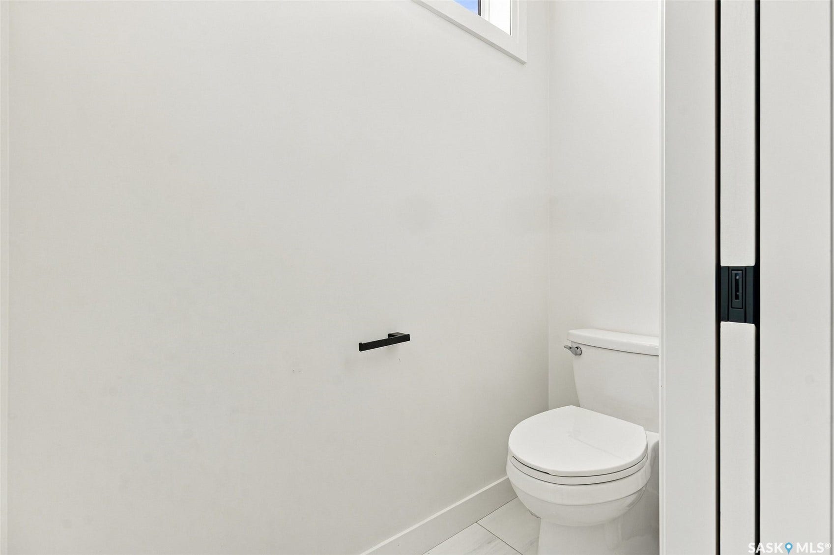 6221 Koep Avenue, Regina SK S4X 0J2 Modern toilet fixture, white ceramic toilet, white wall finishes, white tile flooring, and a black toilet paper holder