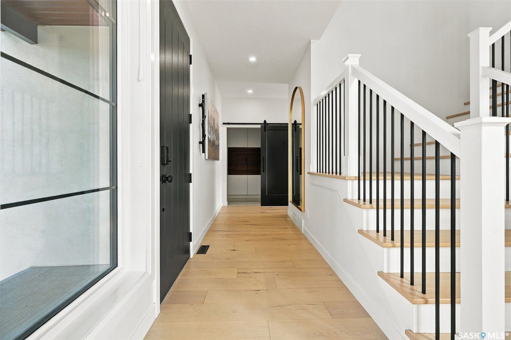 6221 Koep Avenue, Regina SK S4X 0J2 Foyer featuring wood-finish flooring, a contemporary staircase with black metal balusters, and a black paneled door