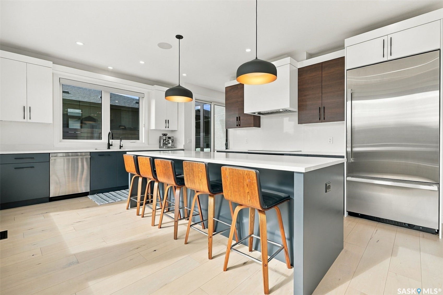 6221 Koep Avenue, Regina SK S4X 0J2 Gourmet kitchen with two-tone cabinetry, a large island with seating, stainless steel appliances, and light wood-finish flooring