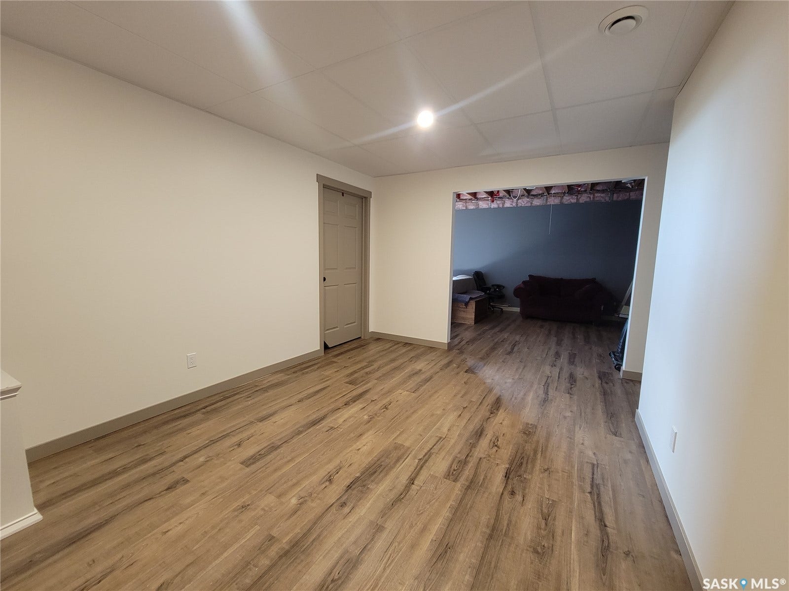 Wood-finish flooring, recessed ceiling lighting, light neutral wall tones, and a paneled interior door