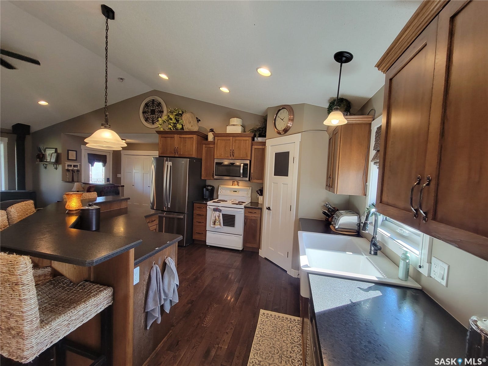 Kitchen featuring wood-finish flooring, dark countertops, wood cabinetry, a white farmhouse sink, and stainless steel appliances