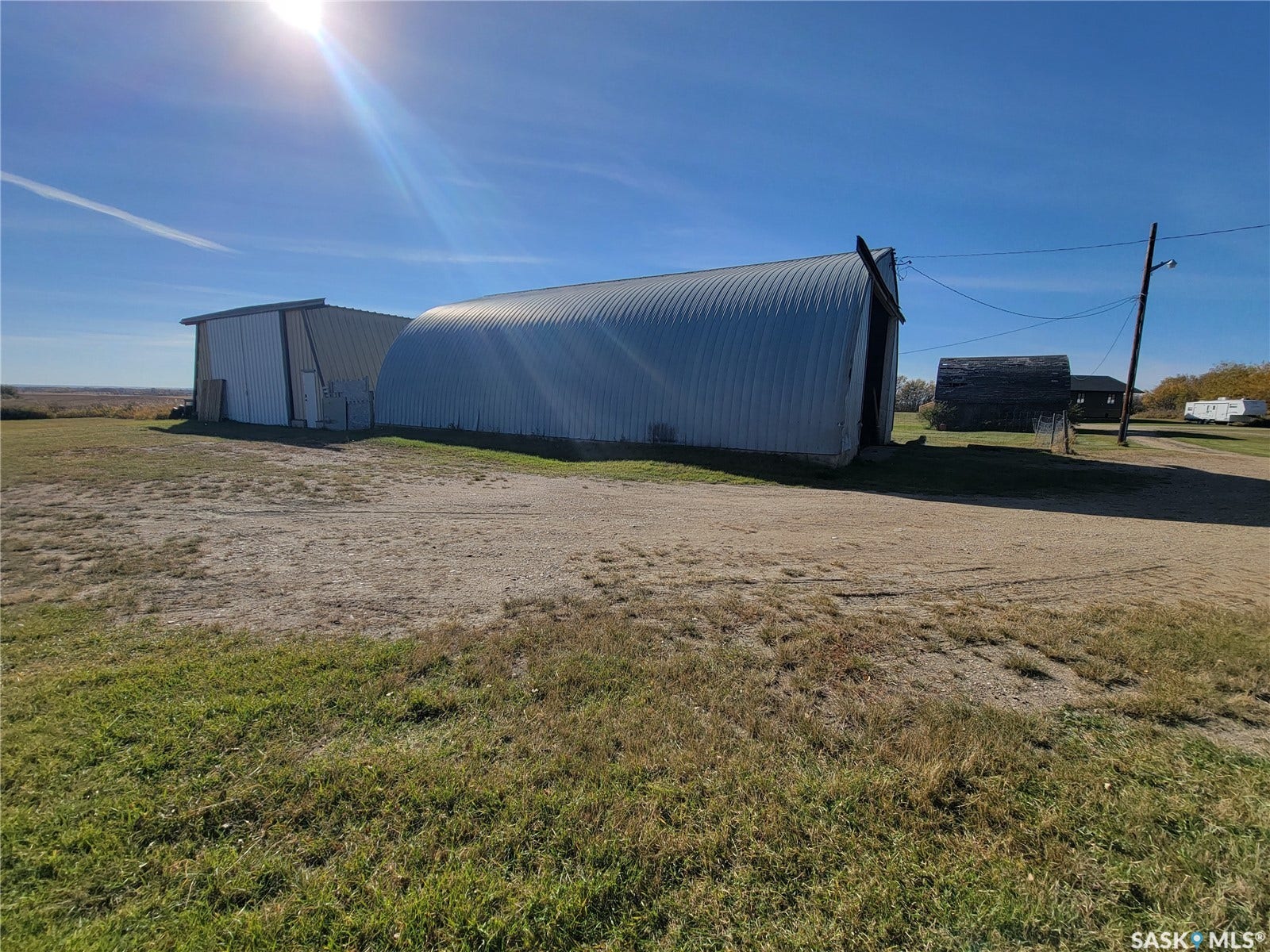 Corrugated metal Quonset hut, white metal-sided building, and large open lot with mixed grass and gravel