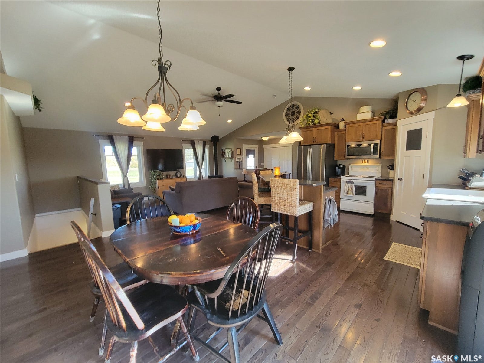 Vaulted ceiling with decorative chandelier, wood-finish flooring, kitchen island with seating, stainless steel appliances, and wood cabinetry