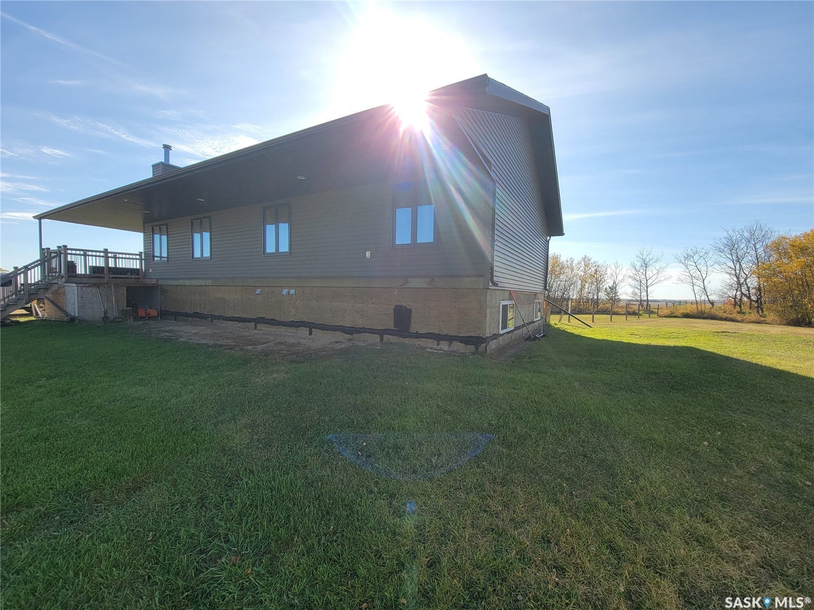 Expansive grassy lawn with a partial wrap-around deck featuring wood railing and stairs