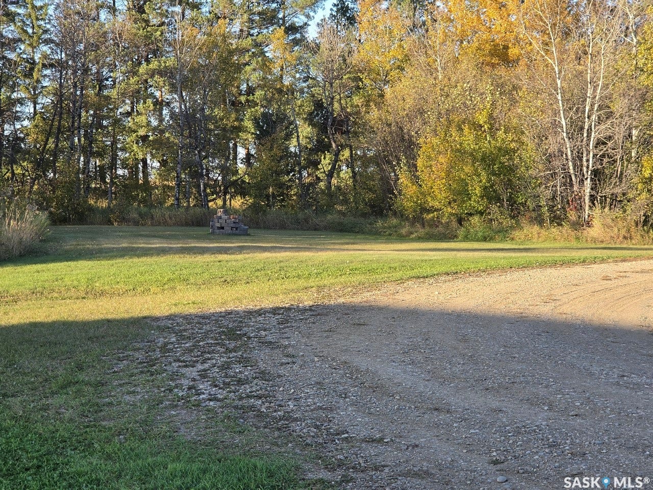 Expansive grass lawn with a gravel access area, bordered by a dense tree line