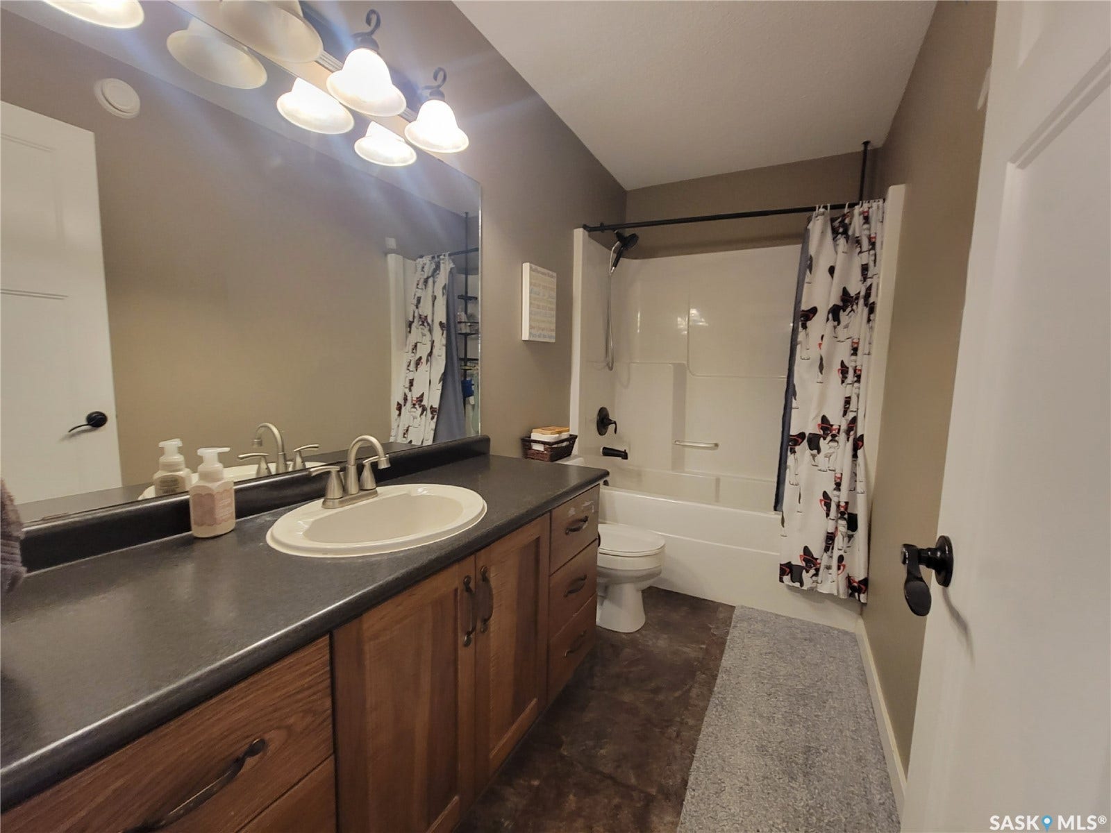 Bathroom featuring a wood-finish vanity with a dark countertop, an integrated sink, and an acrylic tub with a shower