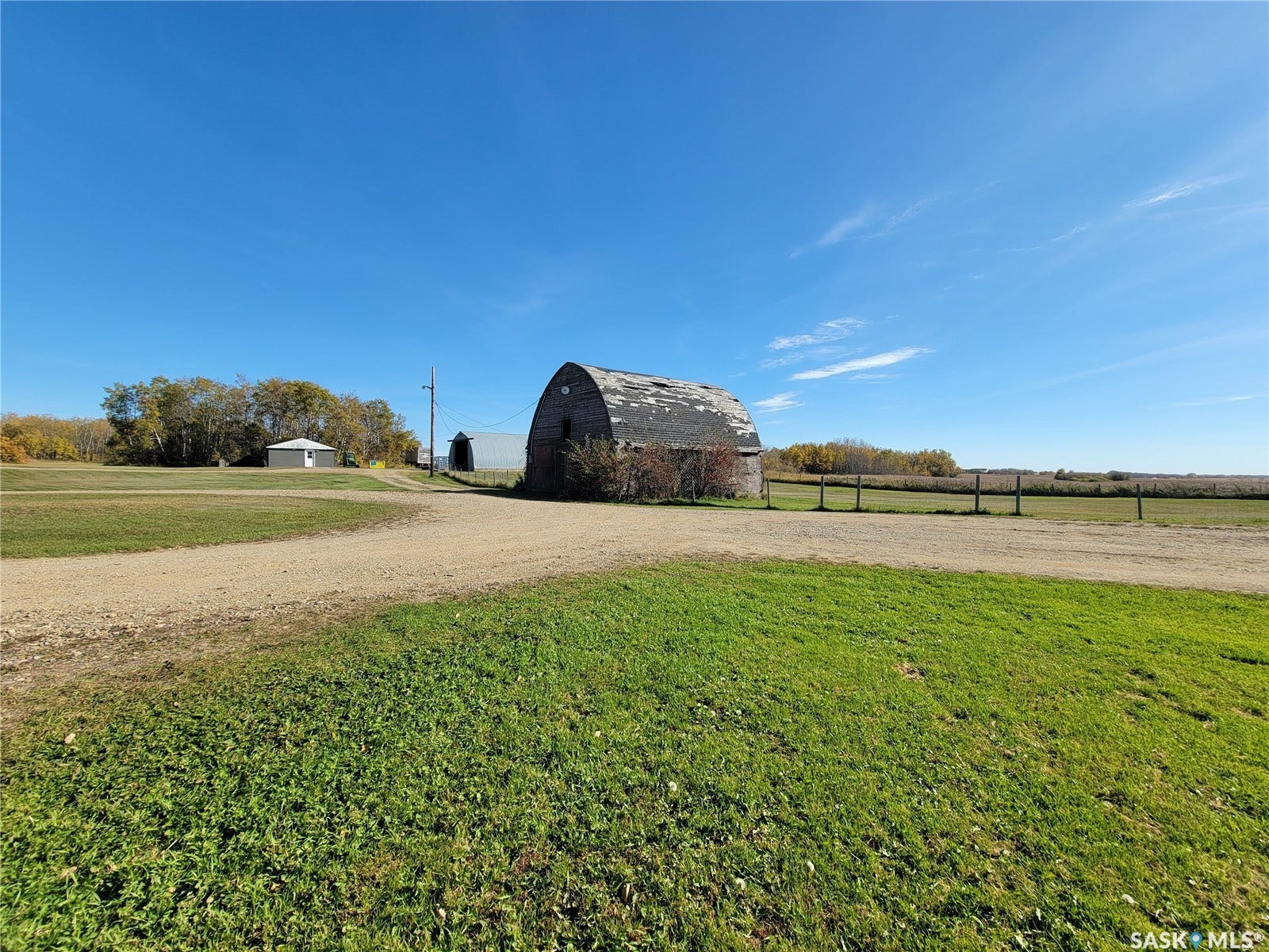 Gravel driveway leading to a weathered barn and outbuildings, surrounded by grassy areas and distant trees