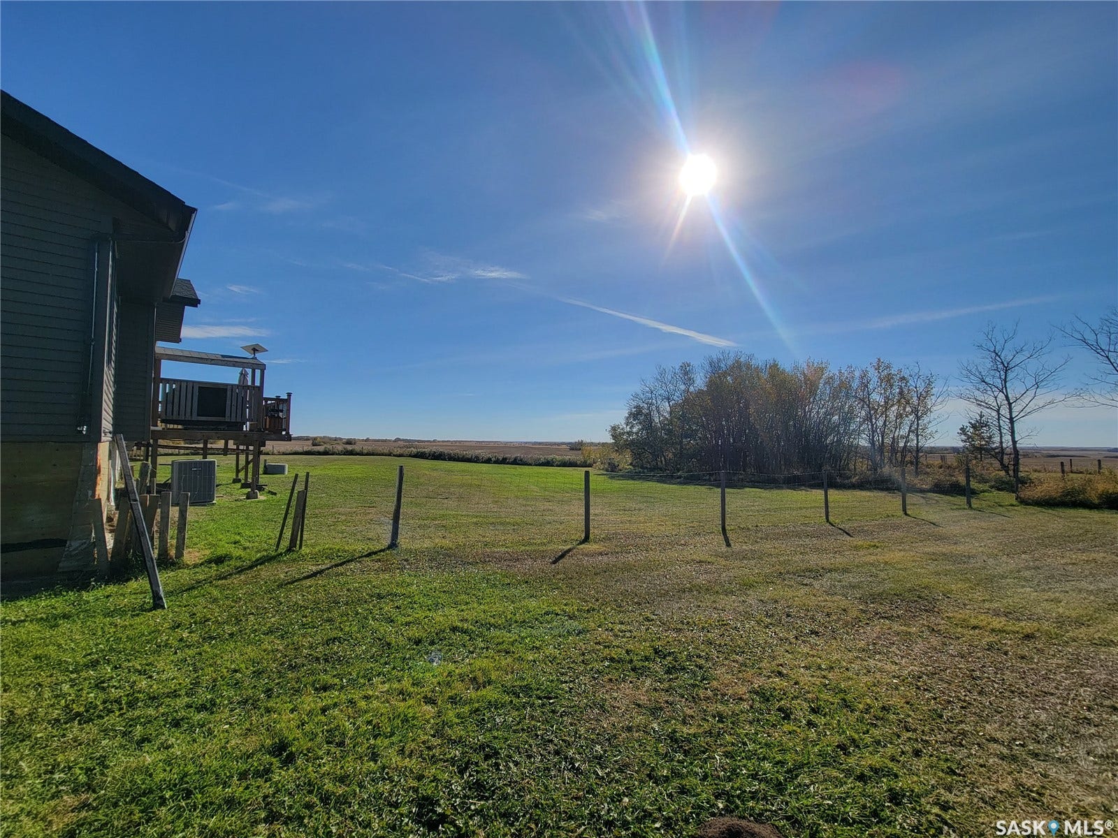 Expansive grassy area with a wooden fence and mature trees