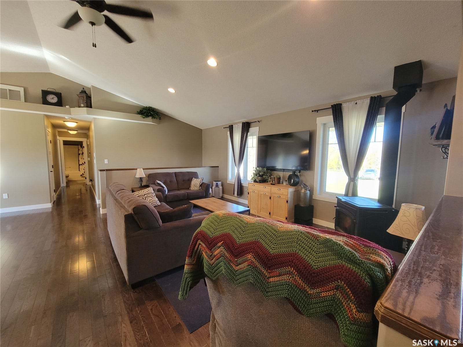 Vaulted ceilings with recessed lighting, wood-finish flooring, and a built-in wood stove with an exposed flue