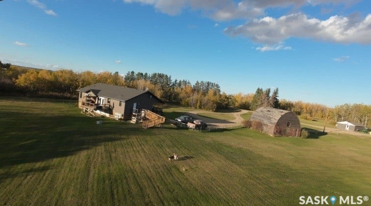 Expansive green lawn surrounding a residence with a multi-level deck, additional outbuilding, and mature trees