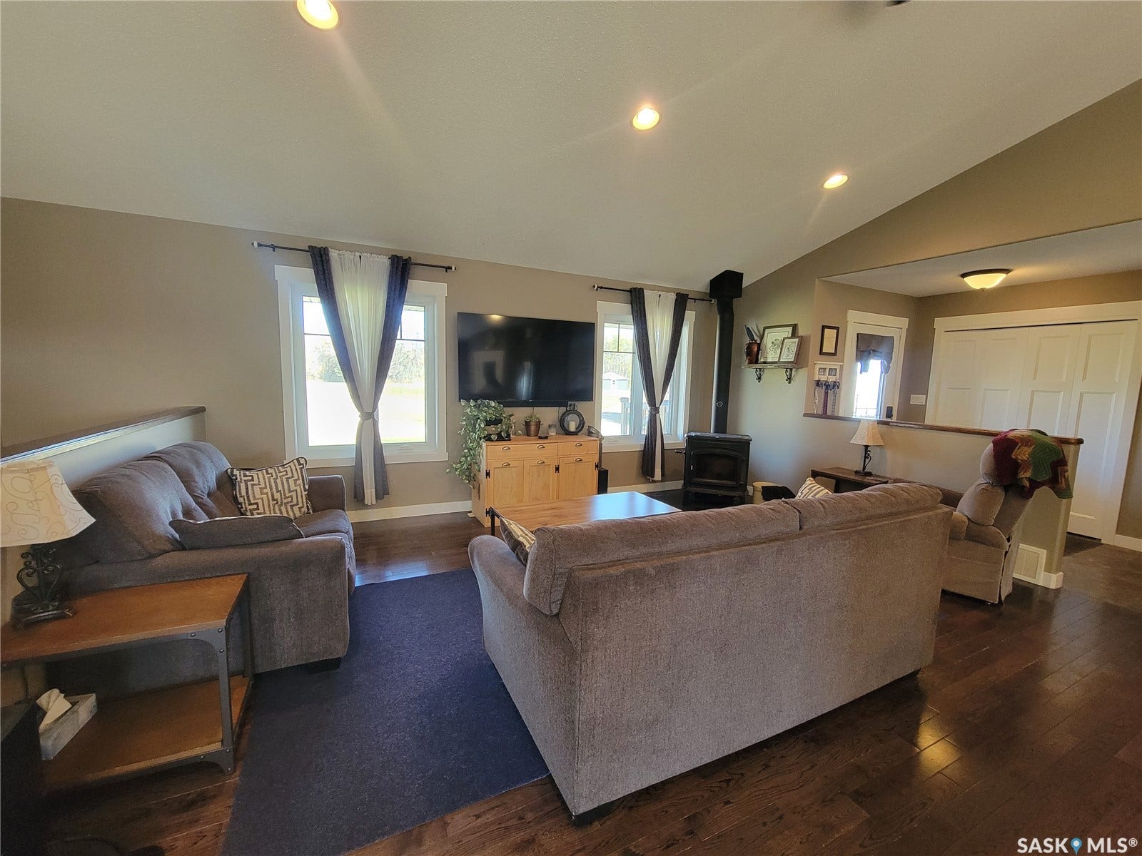Wood-finish flooring with recessed lighting, a vaulted ceiling, and a built-in wood stove