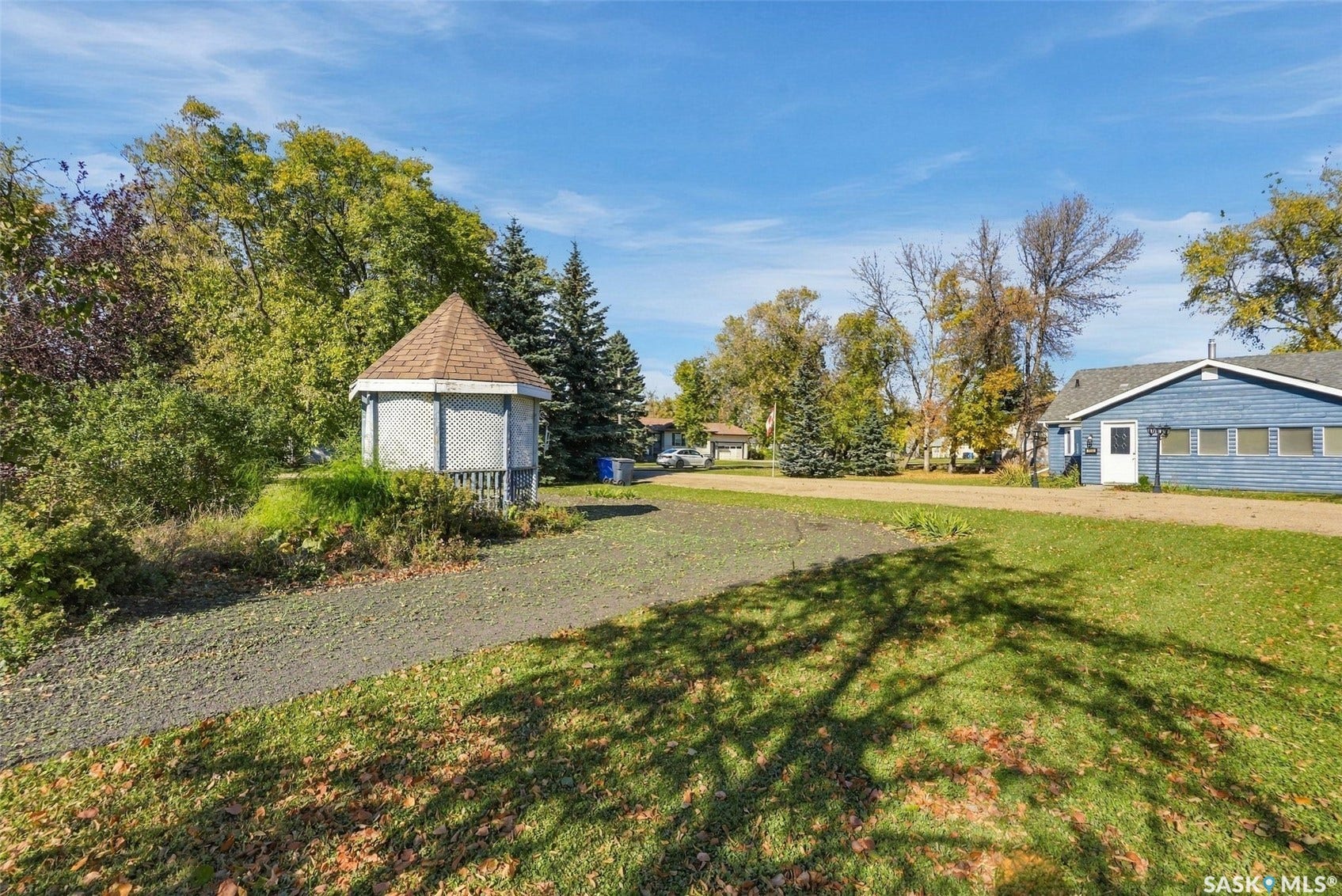 Expansive green lawn with a gazebo featuring a shingled roof, mature trees, and a blue-sided structure