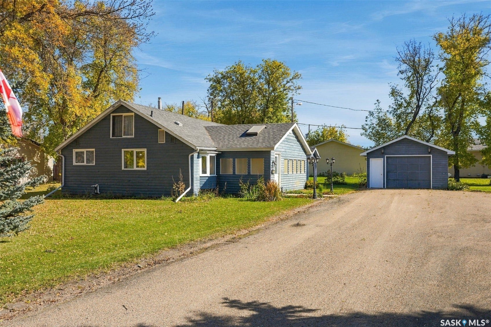 Blue siding exterior with white trim, gray shingle roof, attached sunroom, and detached garage with a roll-up door