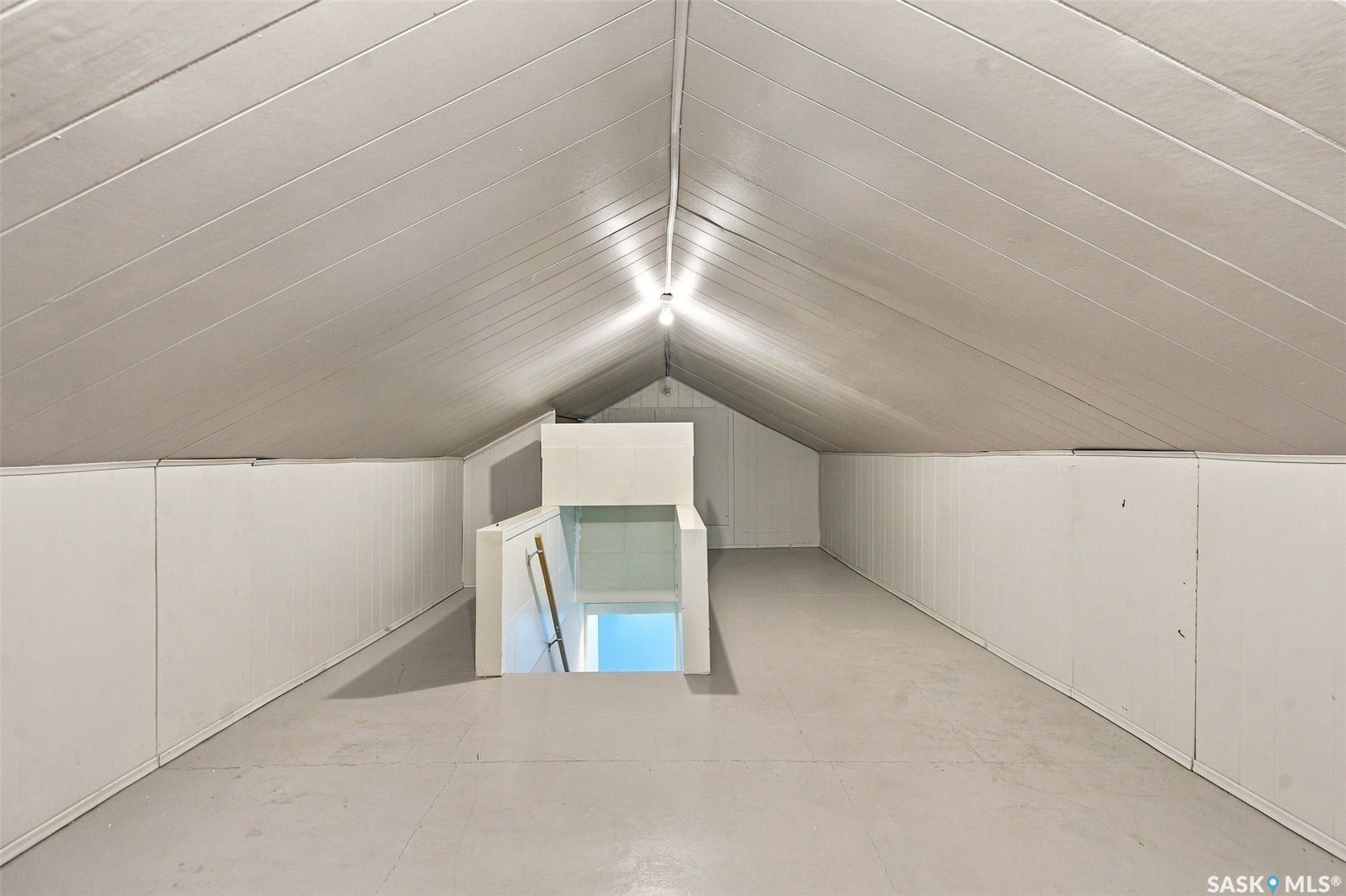 Sloped ceiling with paneled walls and a light-toned floor