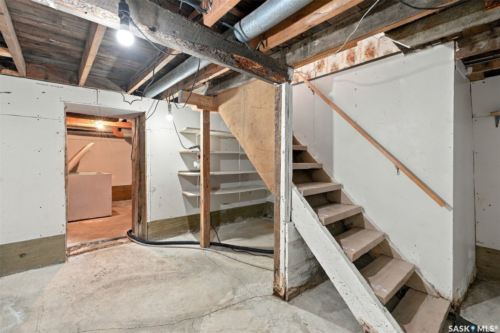 Basement space featuring exposed ceiling joists, concrete flooring, and a wooden staircase with a handrail