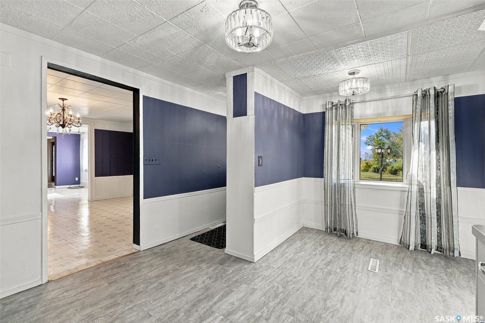 Distinguished interior with patterned ceiling, two crystal-style light fixtures, a window with exterior scenery, and wood-finish flooring