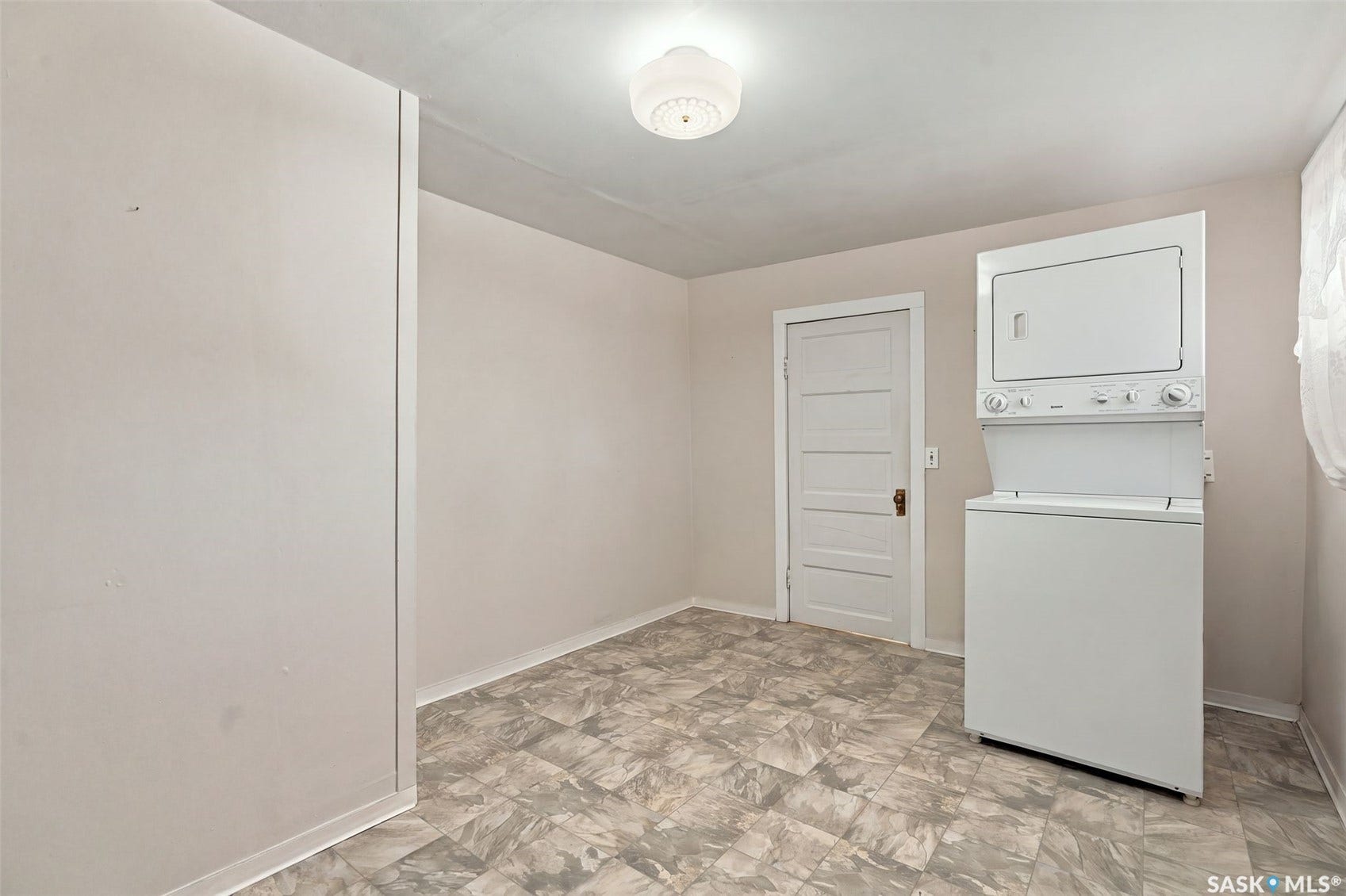 Laundry area with a stacked washer and dryer, vinyl flooring, and a flush-mount ceiling light fixture