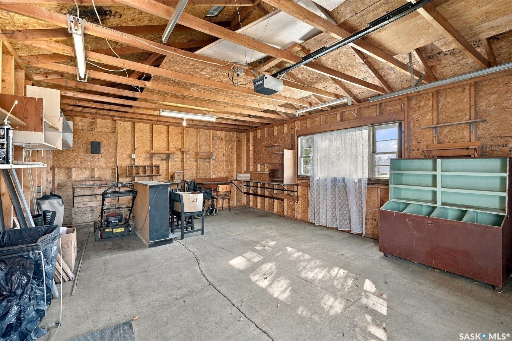 Attached garage featuring exposed wood beam ceiling, concrete flooring, and built-in shelving