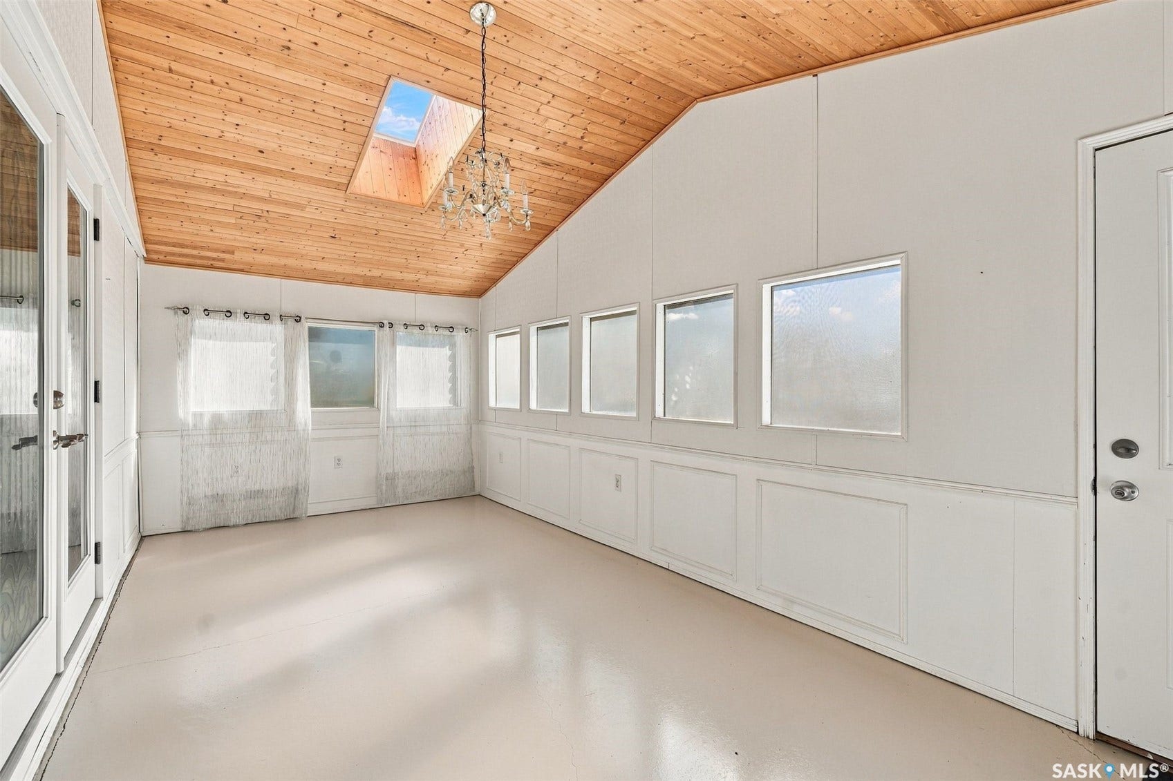 Vaulted wood-paneled ceiling with a skylight and chandelier, multiple windows, and a panelled wall