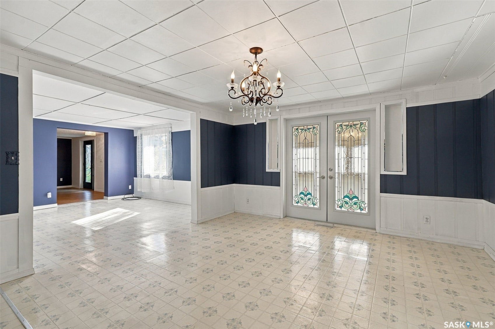 Tiled flooring, double doors with decorative glass inserts, wall paneling, built-in wall niches, and an ornate chandelier