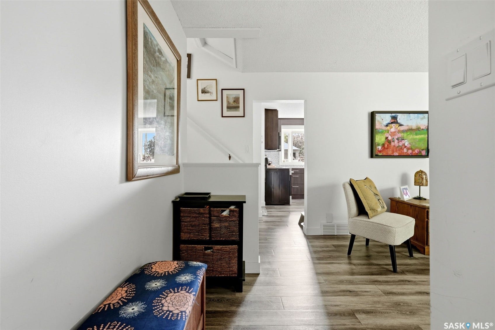 Wood-finish flooring throughout, white painted walls, and an open doorway to the kitchen