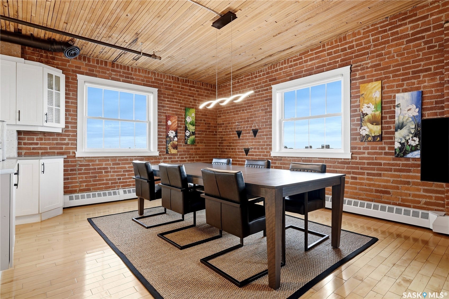 Exposed brick walls, wood-finish ceiling, light wood-finish flooring, white cabinetry with dark hardware, and double-hung windows