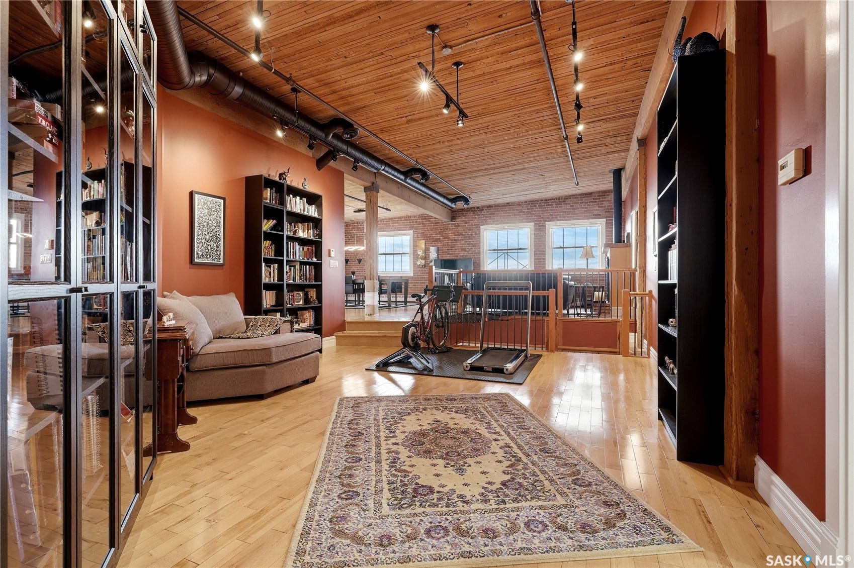 Hardwood flooring with exposed wood ceiling beams, track lighting, and a loft layout