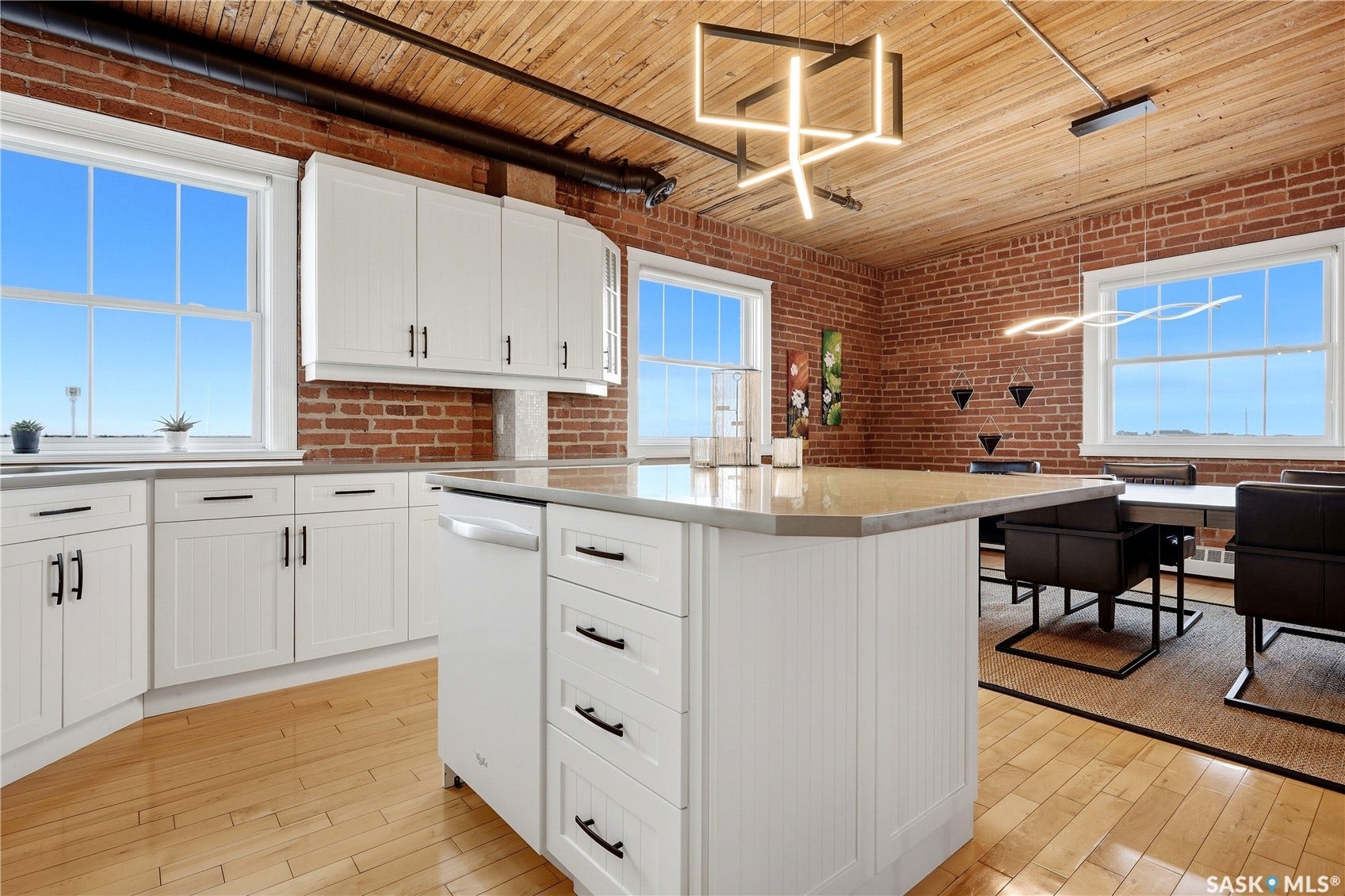 White shaker-style cabinetry with black hardware, wood-finish flooring, exposed brick walls, and a wood-paneled ceiling