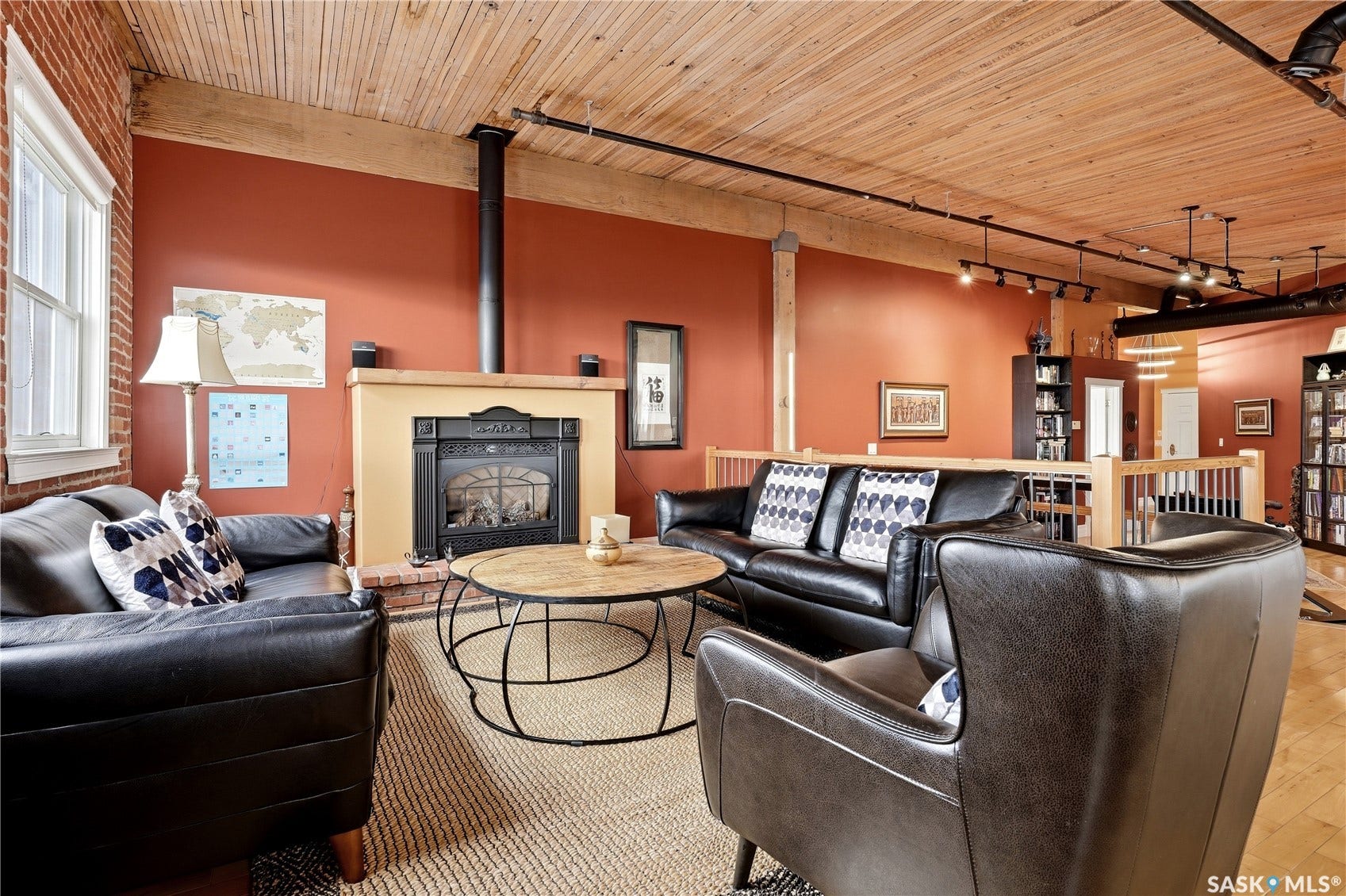 Exposed brick wall, natural wood ceiling, fireplace with mantel, track lighting, and wood-finish flooring