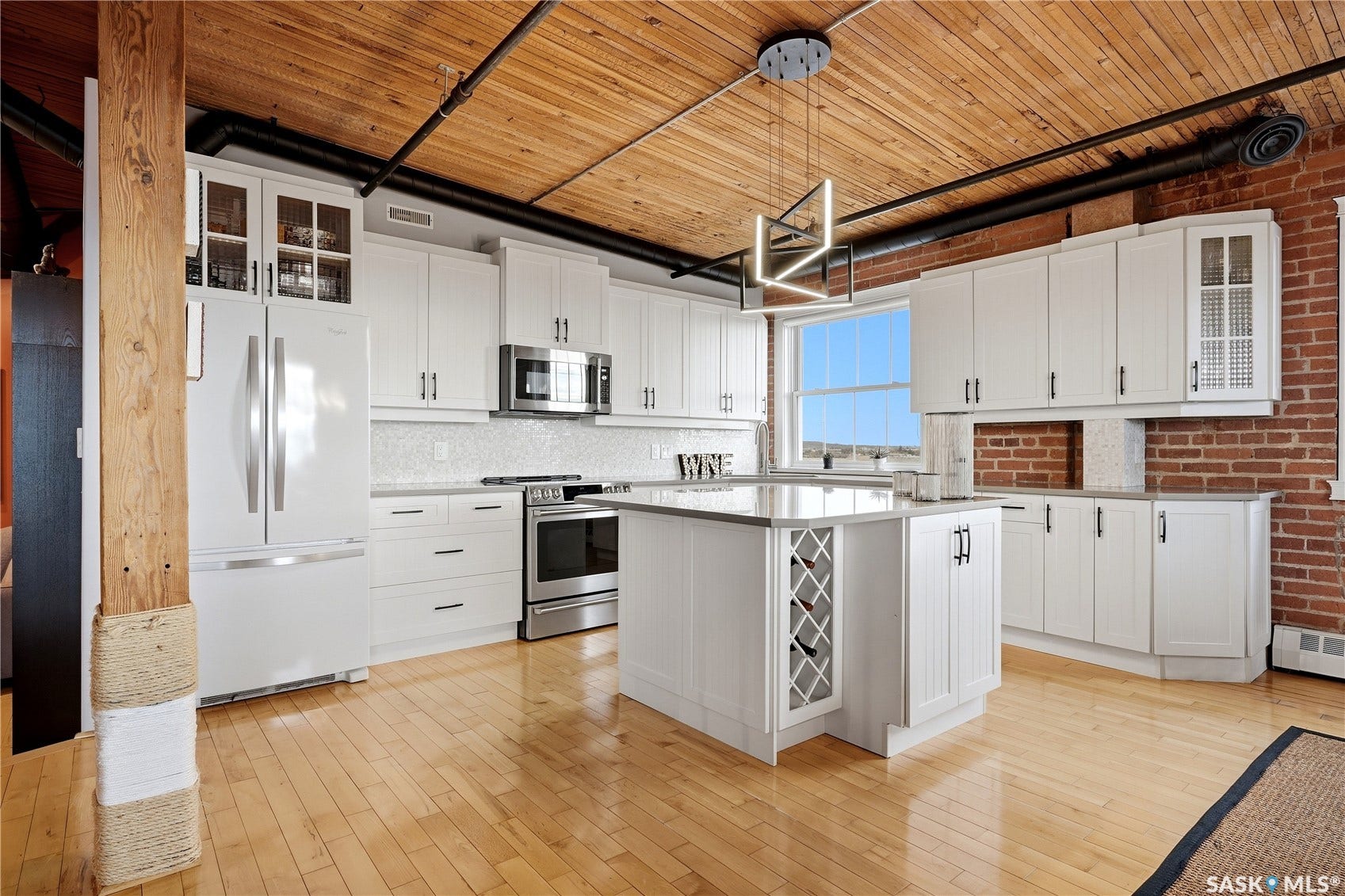 White cabinetry with dark hardware, stainless steel appliances, light wood-finish flooring, exposed brick wall, and a wood-panel ceiling