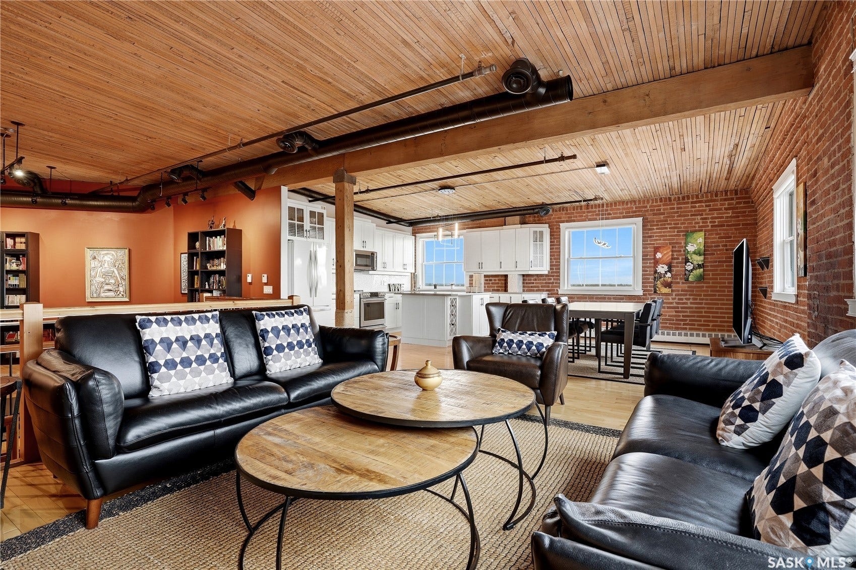 Exposed brick walls, wood-finish ceiling, hardwood flooring, white cabinetry, and large windows