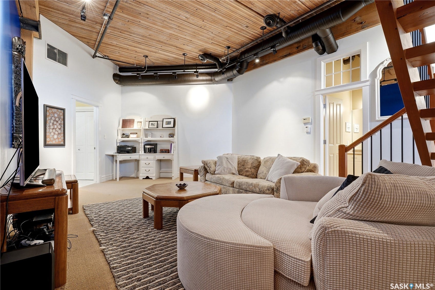 Vaulted wood-plank ceiling with exposed ductwork, track lighting, and a built-in desk unit