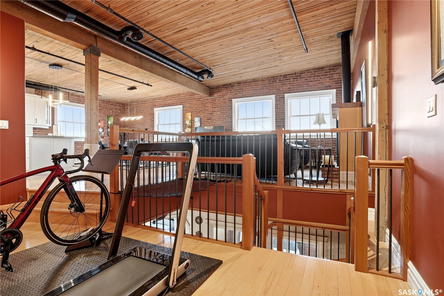 Exposed brick wall, natural wood ceiling, wood support beams, hardwood flooring, and wrought iron railings