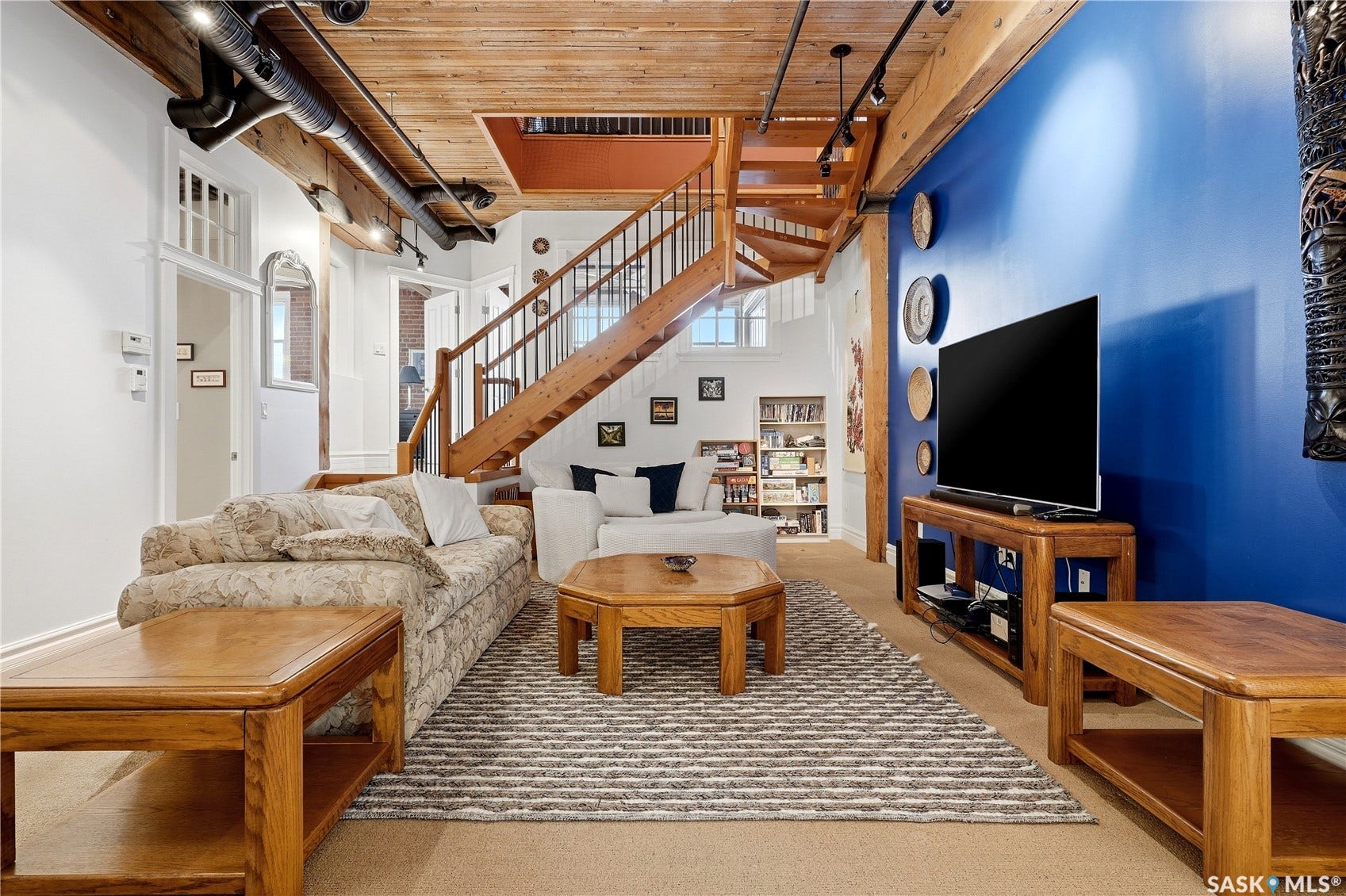 Exposed wood beam ceiling, open-tread wood staircase with metal balusters, and industrial-style exposed ductwork