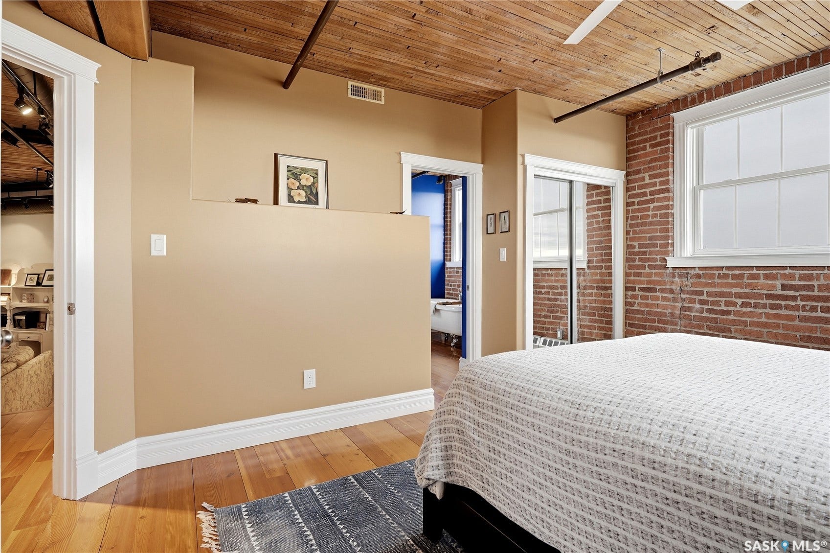 Exposed brick wall, natural wood ceiling, wood-finish flooring, white window frame, and mirrored sliding closet doors