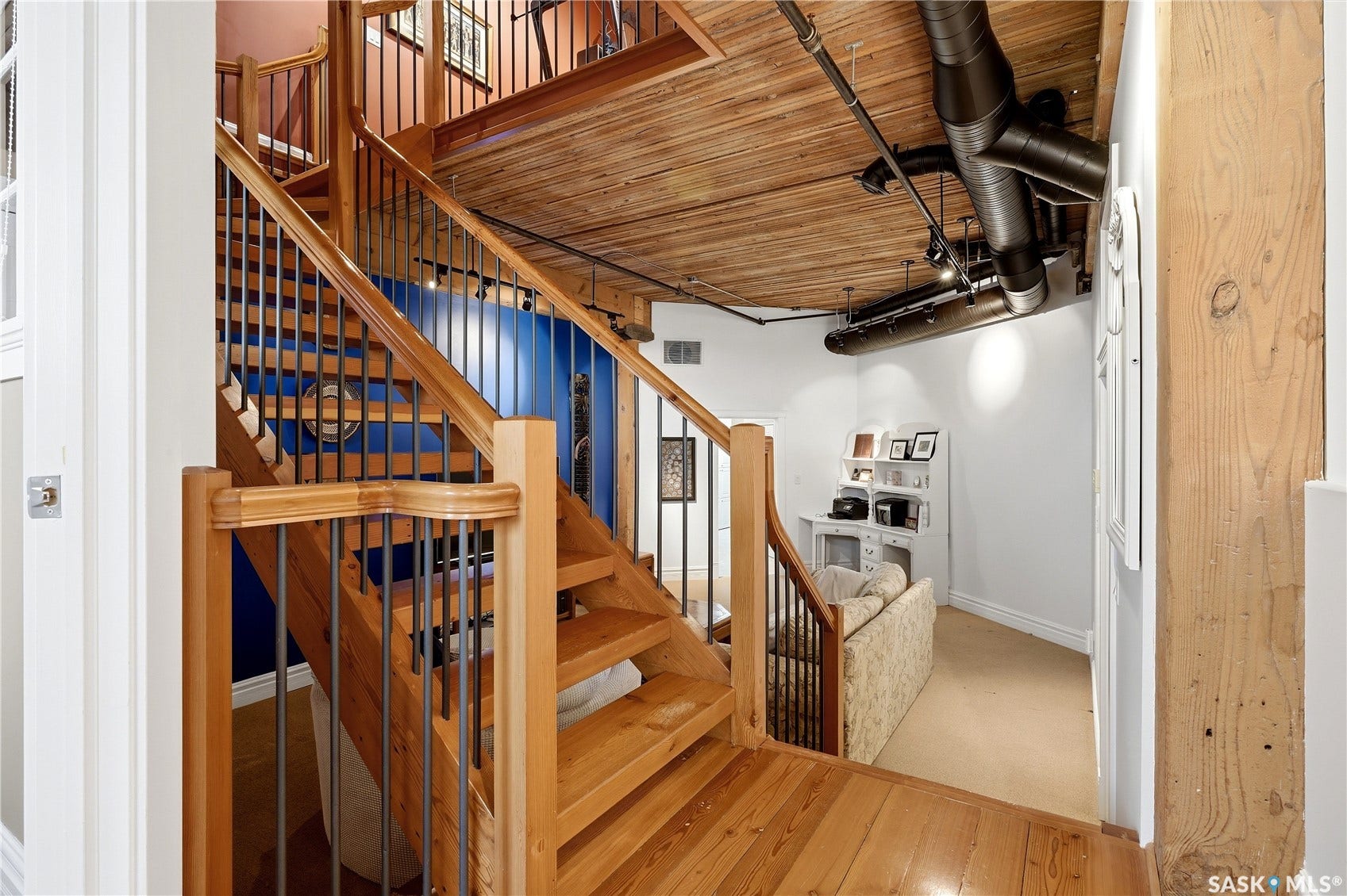 Hardwood flooring, exposed wood beam ceiling, open-tread staircase with metal balusters, and exposed ductwork