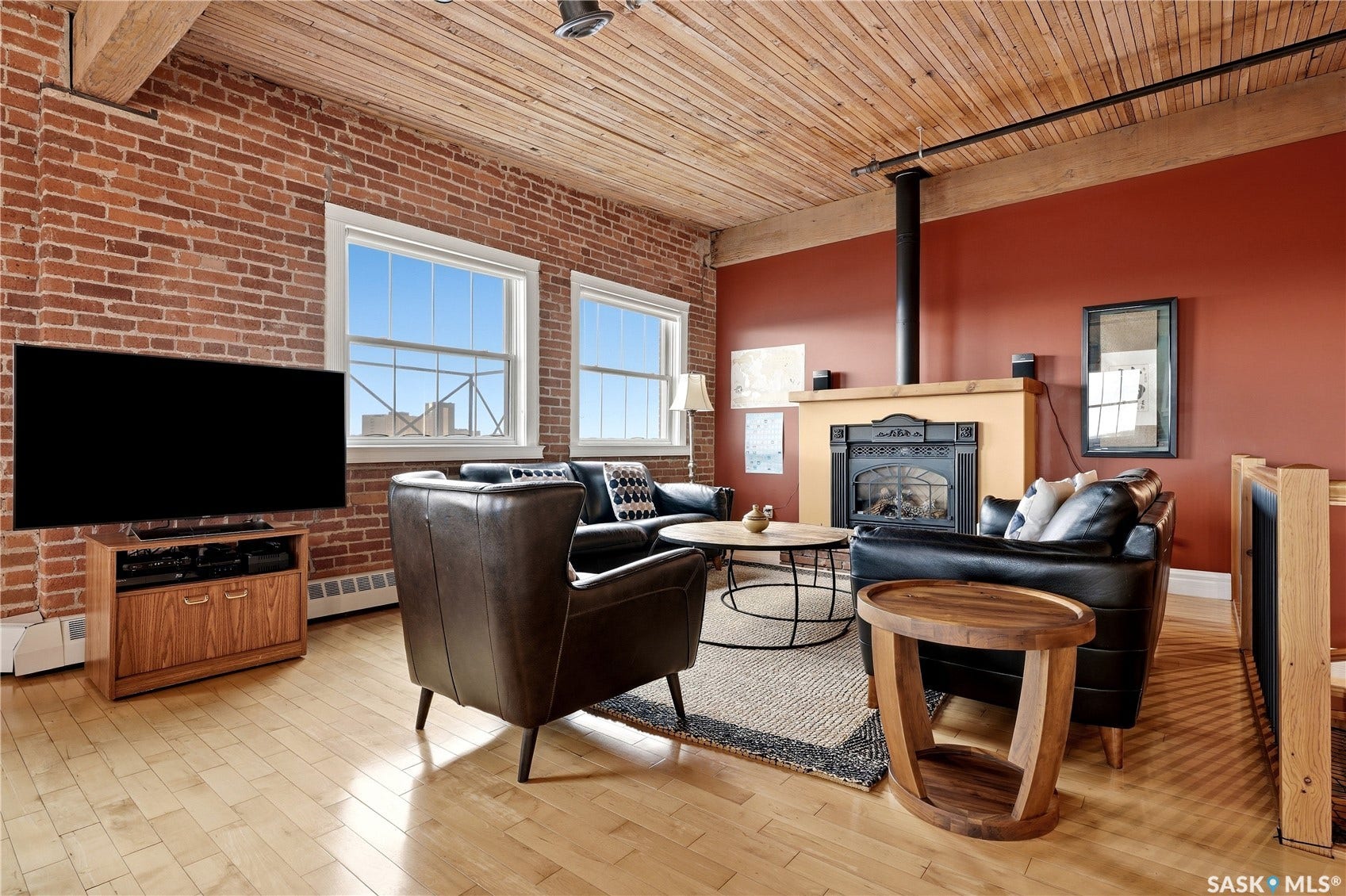 Exposed brick wall, light wood-finish flooring, wood plank ceiling, fireplace with mantel, and two large windows