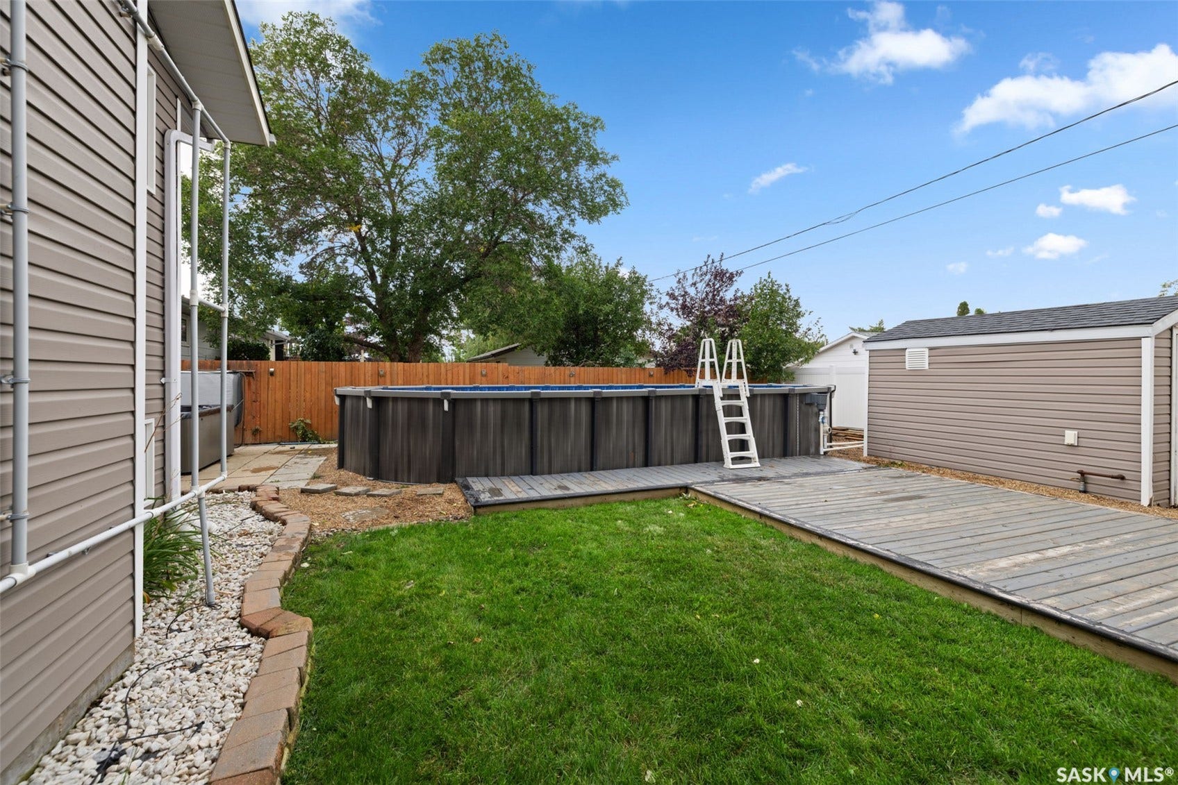 Expansive backyard featuring a manicured lawn, above-ground pool, and wood-finish decking