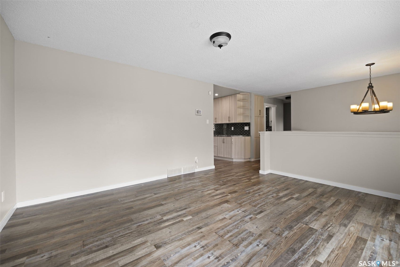 Wood-finish flooring with a neutral wall color, semi-flush ceiling light, and an iron chandelier