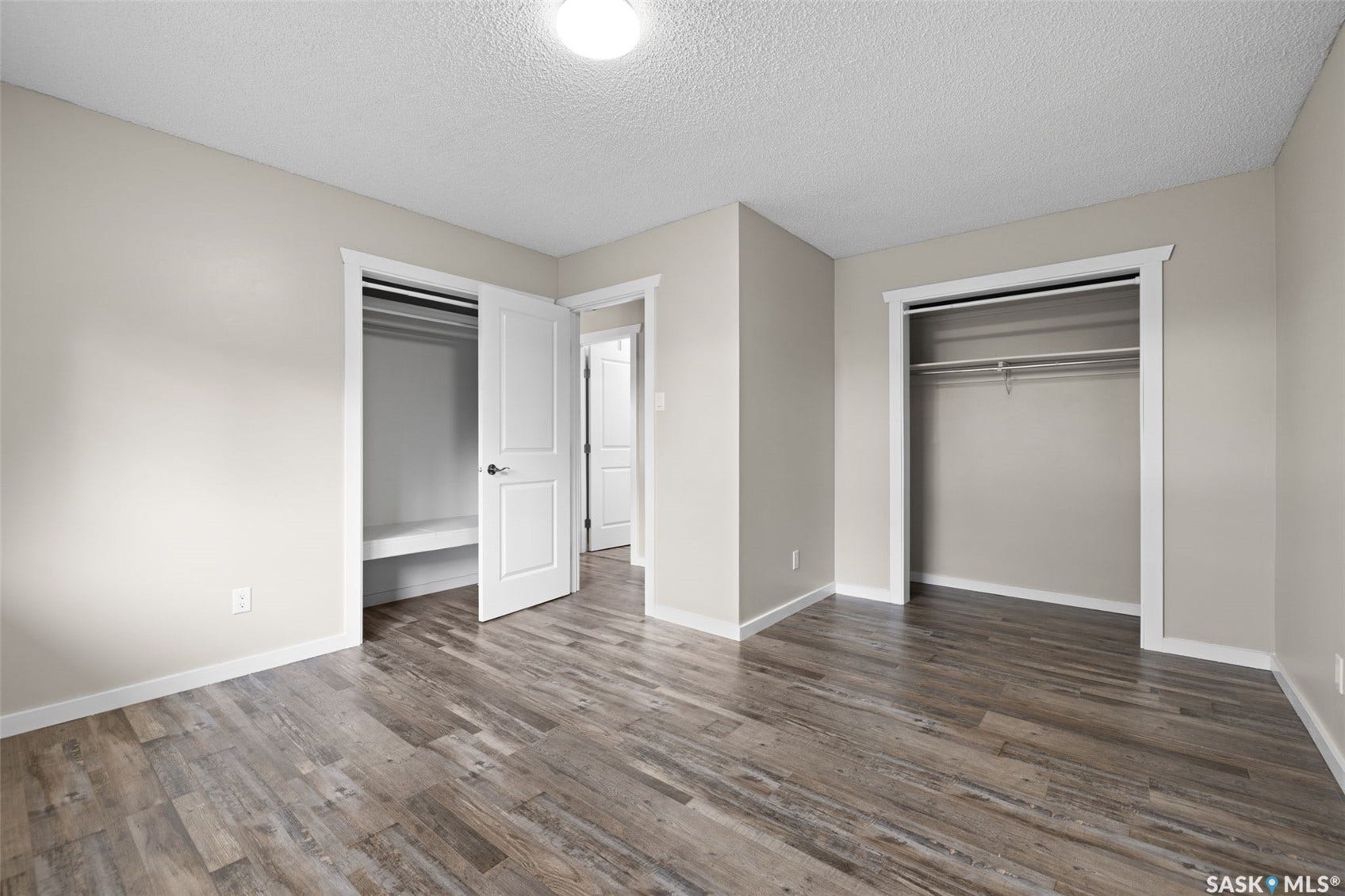 Wood-finish flooring, neutral wall paint, overhead lighting, and two built-in closets with shelving and hanging rods