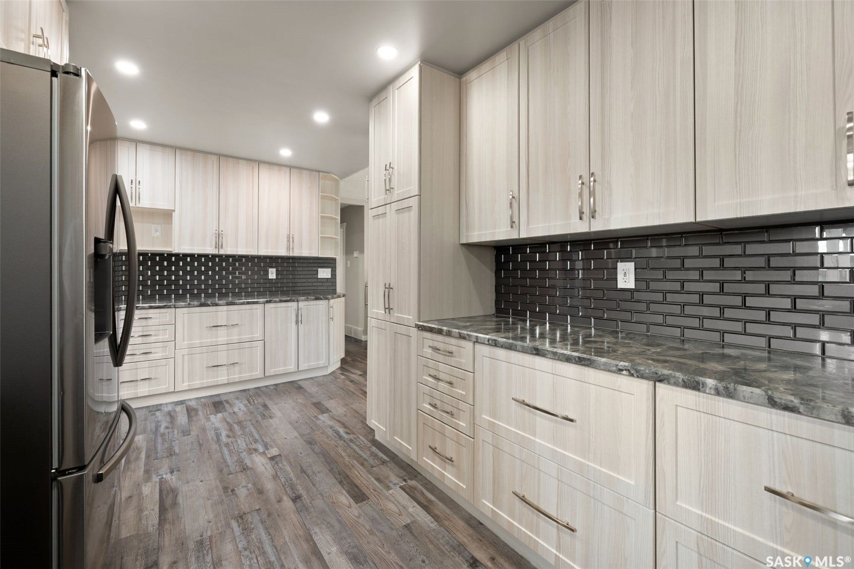 Kitchen featuring wood-finish flooring, recessed lighting, light-toned cabinetry with metal hardware, a dark subway tile backsplash, and stone countertops
