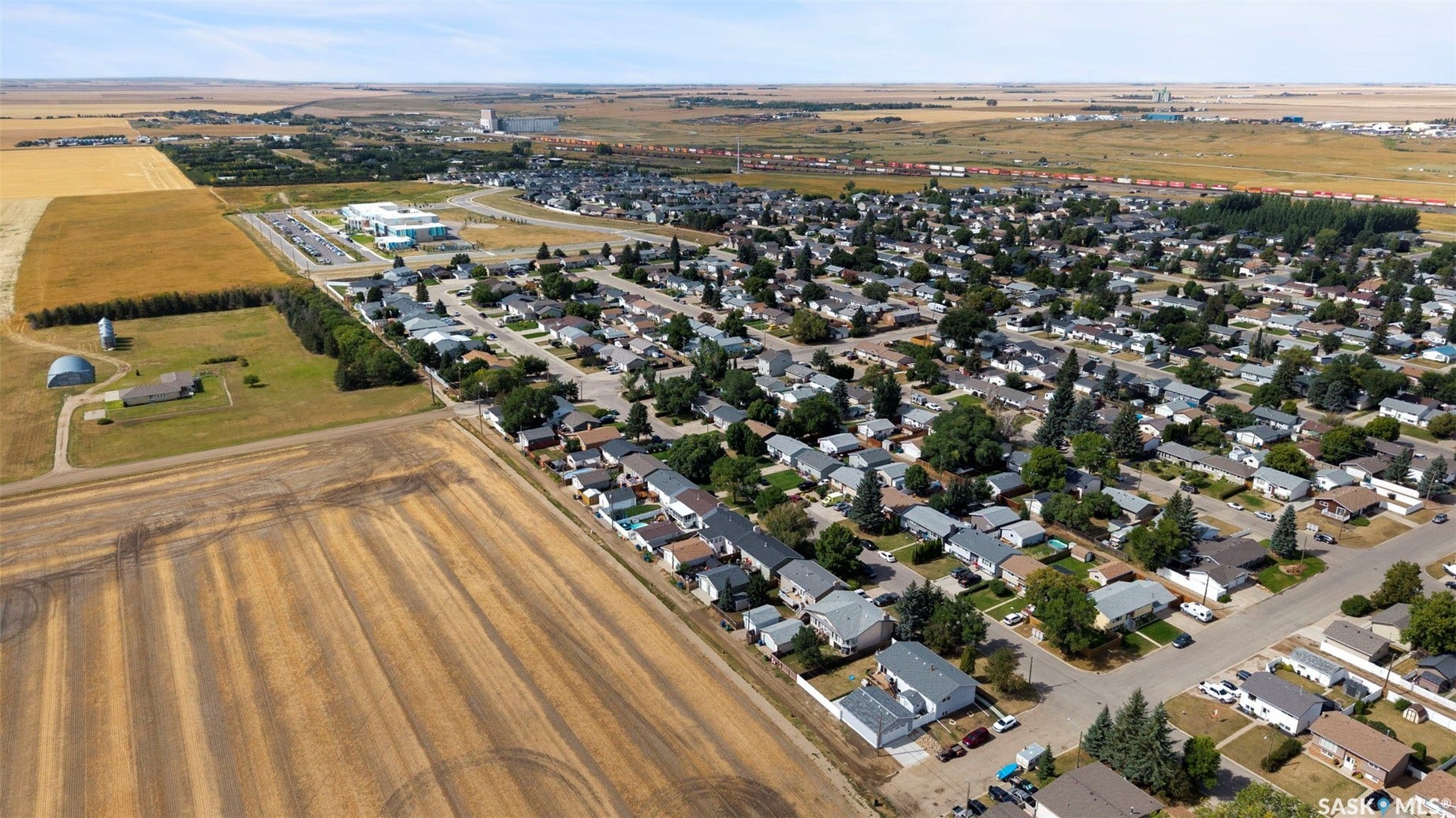 Expansive agricultural fields with residential development, commercial structures, and distant industrial buildings
