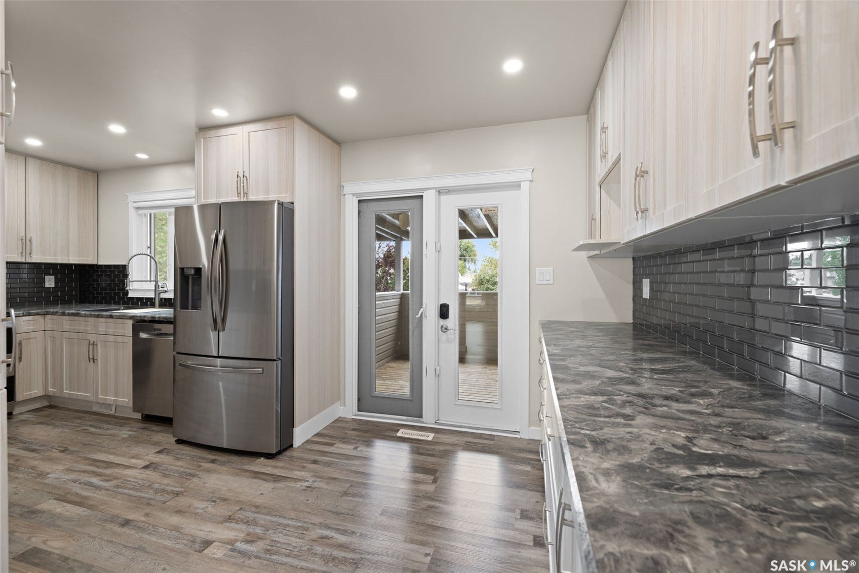 Wood-finish flooring, light-toned cabinetry, dark patterned countertops, and a dark subway tile backsplash
